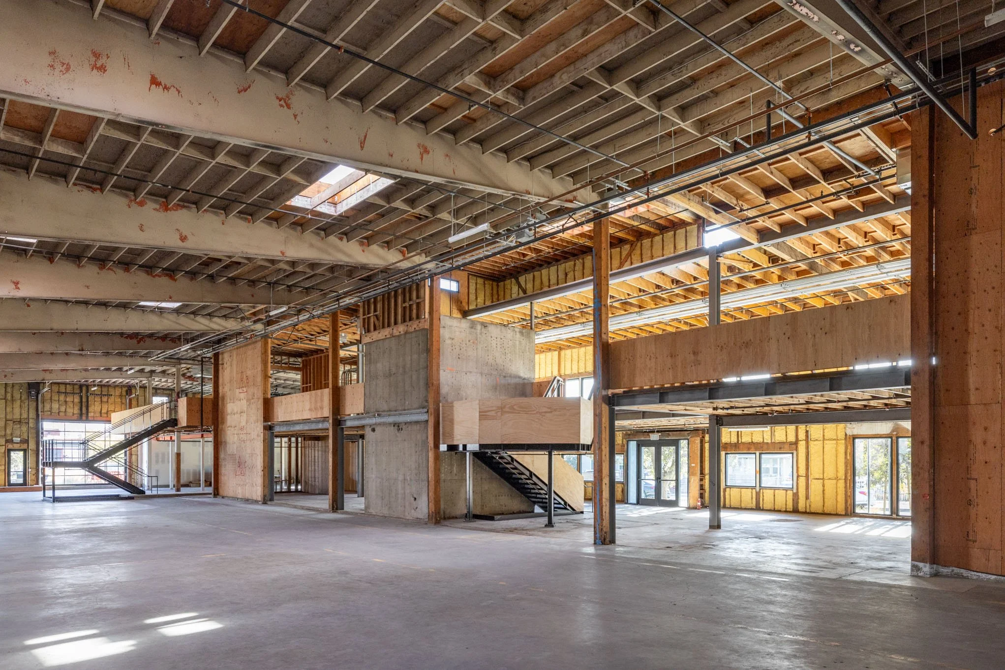 Interior of a building under construction with exposed wooden framing, concrete walls, and large windows.