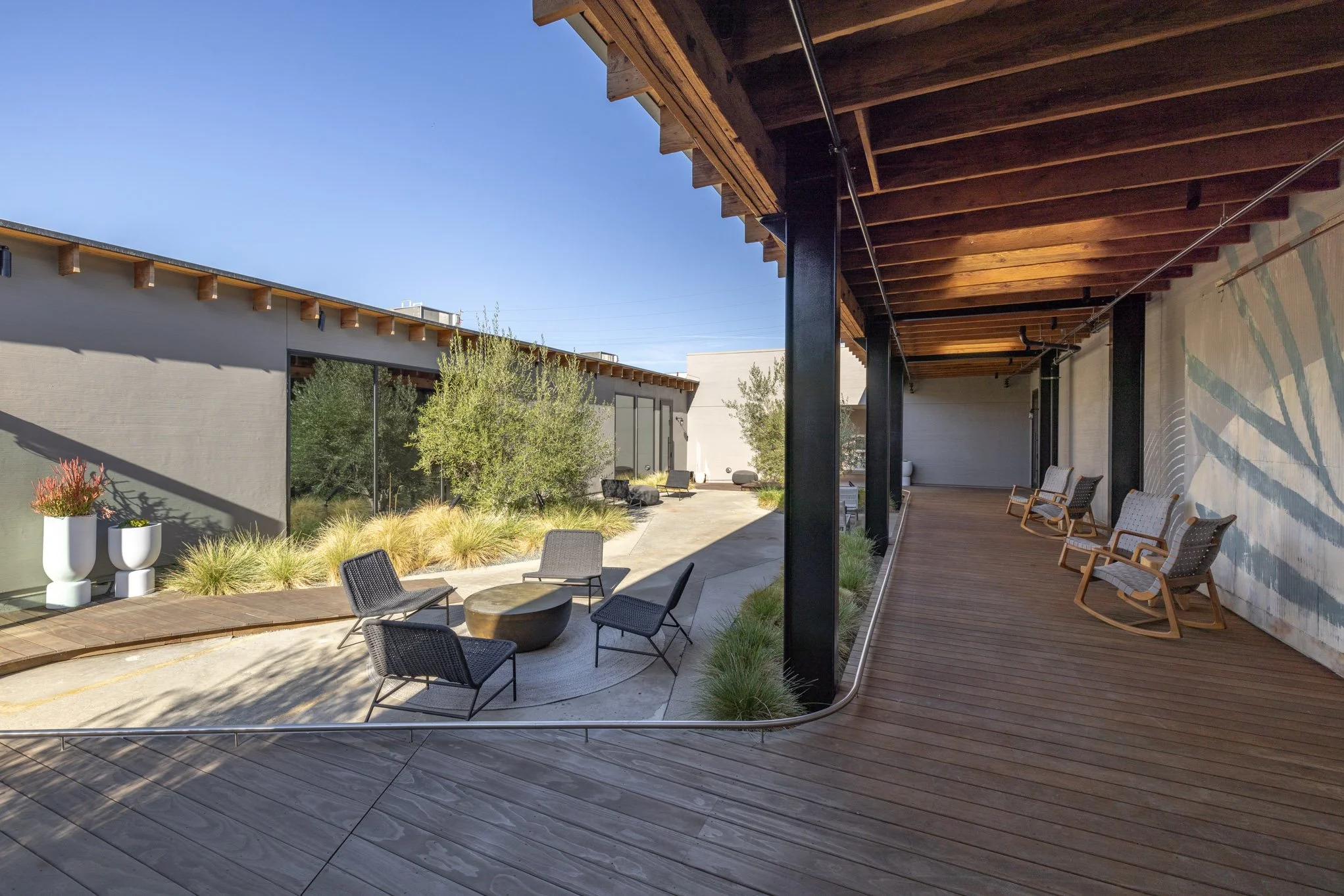 Outdoor patio with wooden deck and modern seating area, surrounded by trees and shrubs, under a clear blue sky.