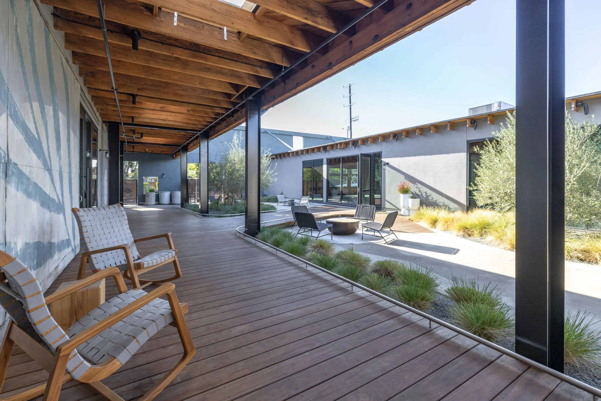 Outdoor patio with wooden deck, modern chairs, and landscaped garden area under a wooden ceiling with black support beams.