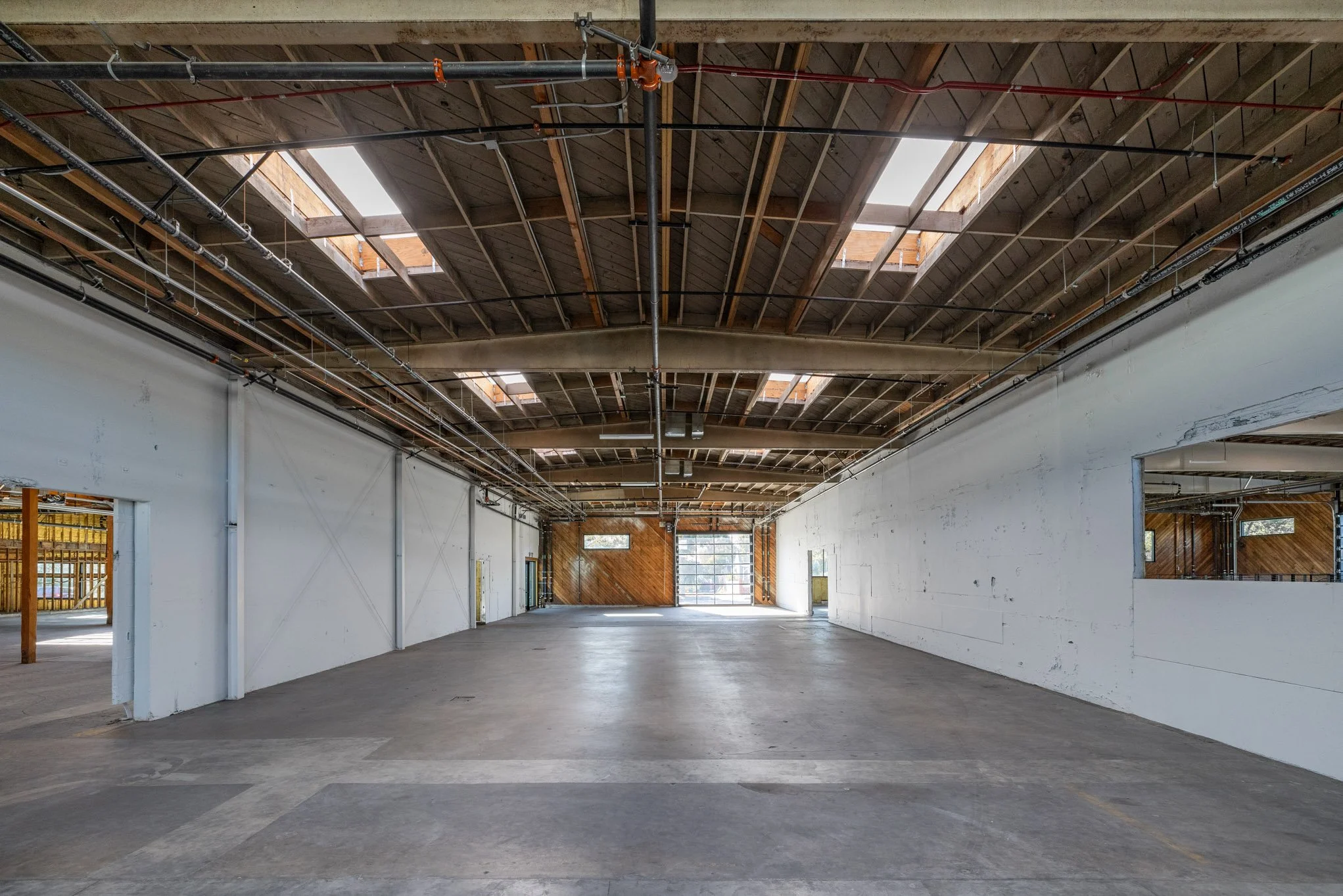 Empty industrial warehouse with high wooden ceiling, skylights, and concrete floor.