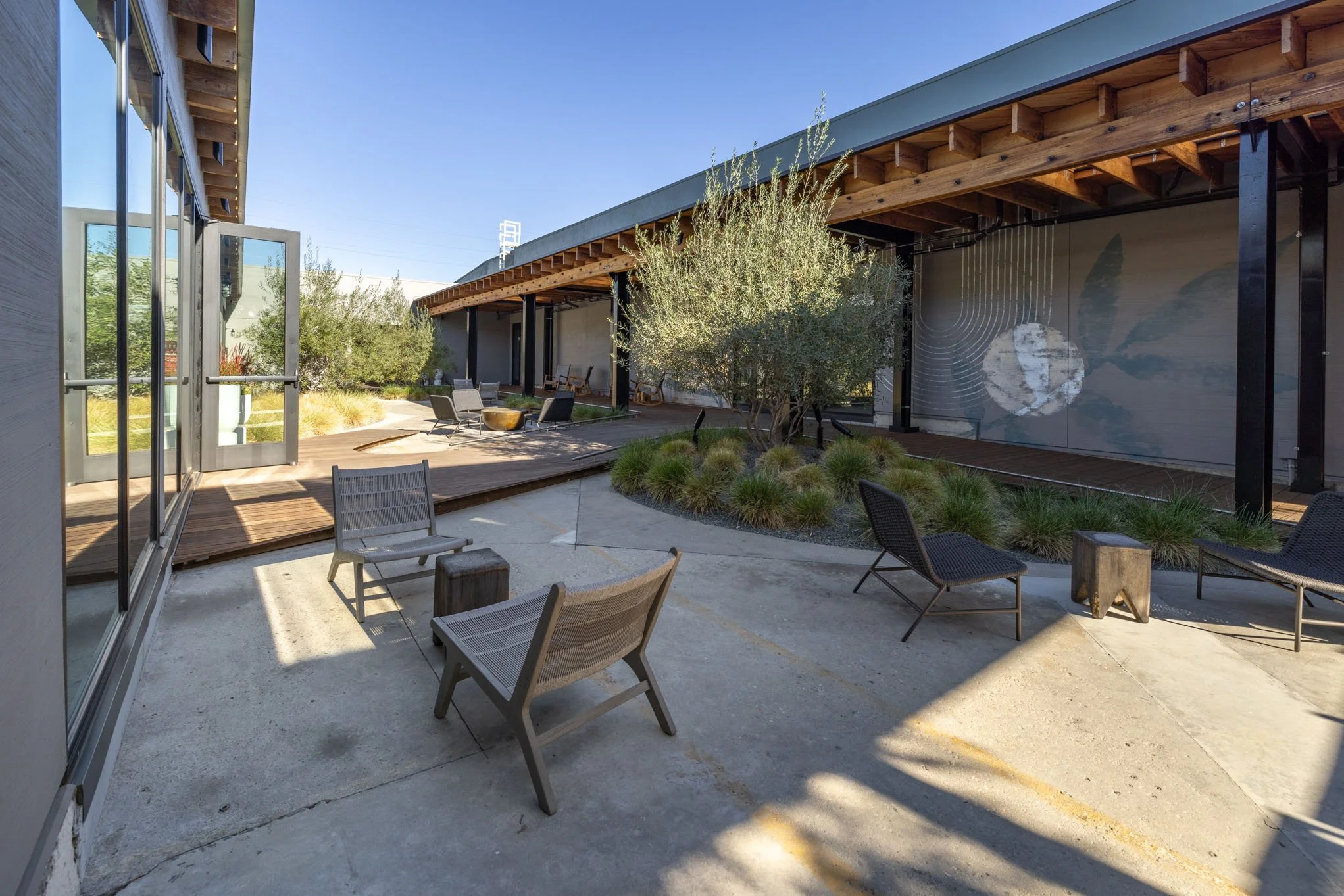 Modern outdoor patio with lounge chairs, trees, and a mural wall under a clear blue sky.