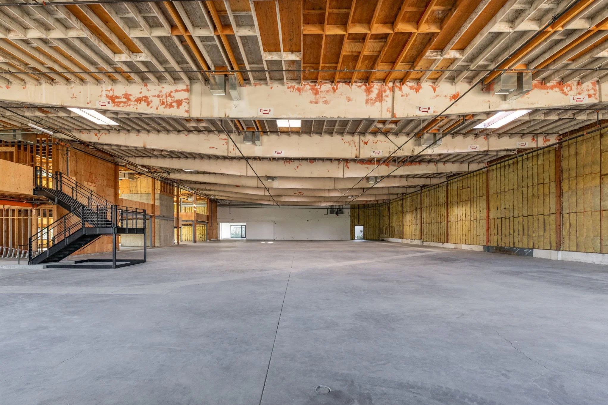 Empty commercial building interior under construction with exposed ceiling beams and insulation on walls.