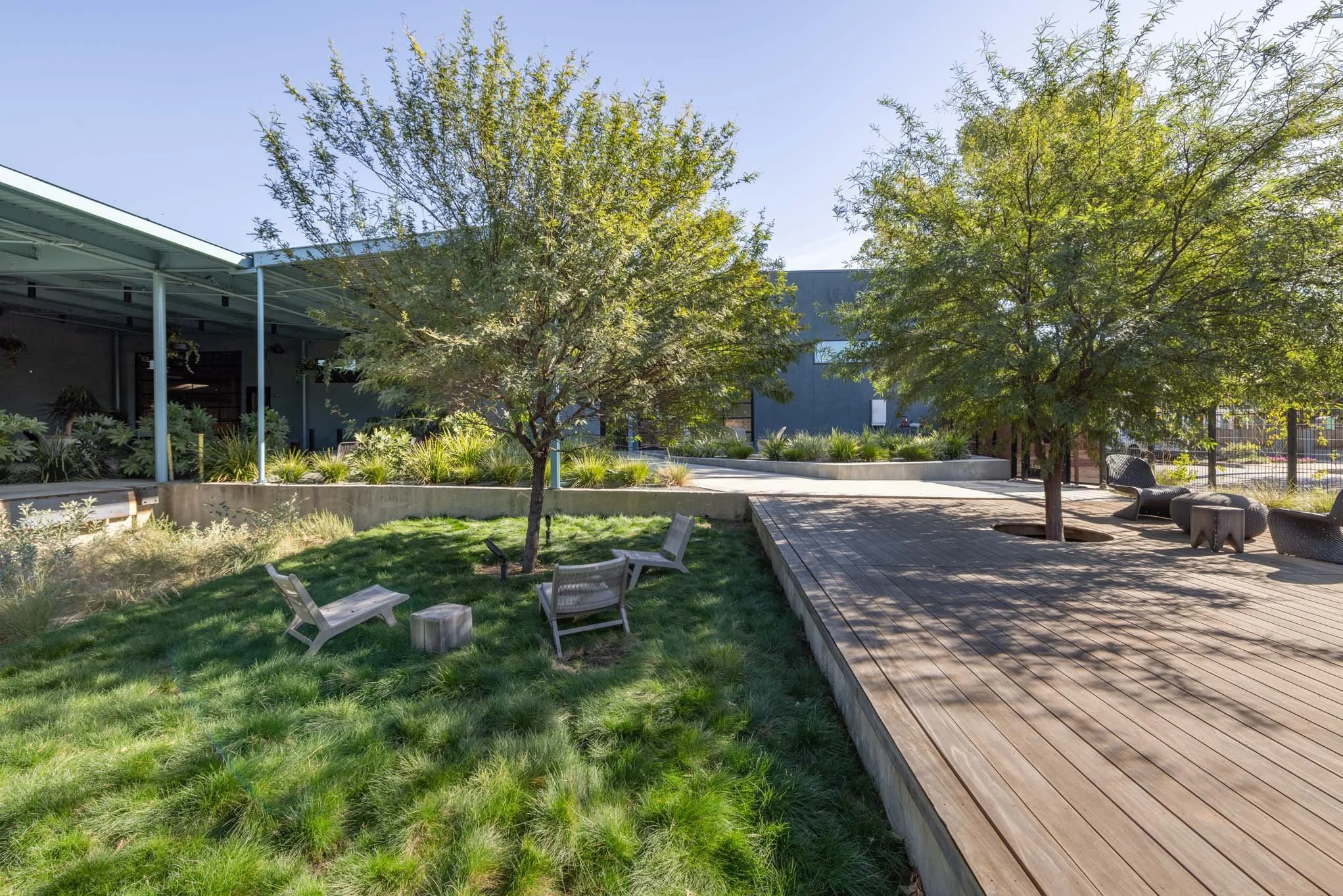 Outdoor park with green grass, trees, wooden benches, and a wooden deck area under sunlight.