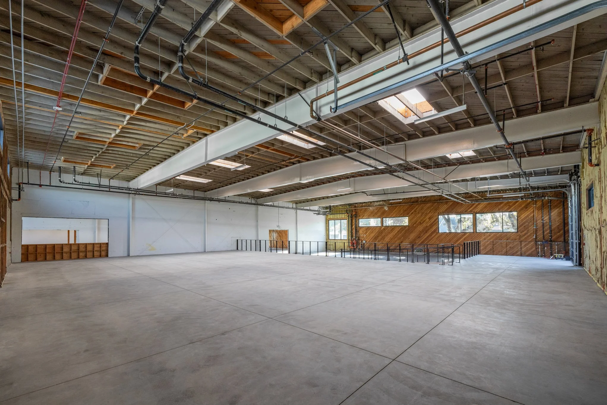 Empty industrial-style indoor space under construction with exposed ceiling beams, HVAC ducts, skylights, and windows.
