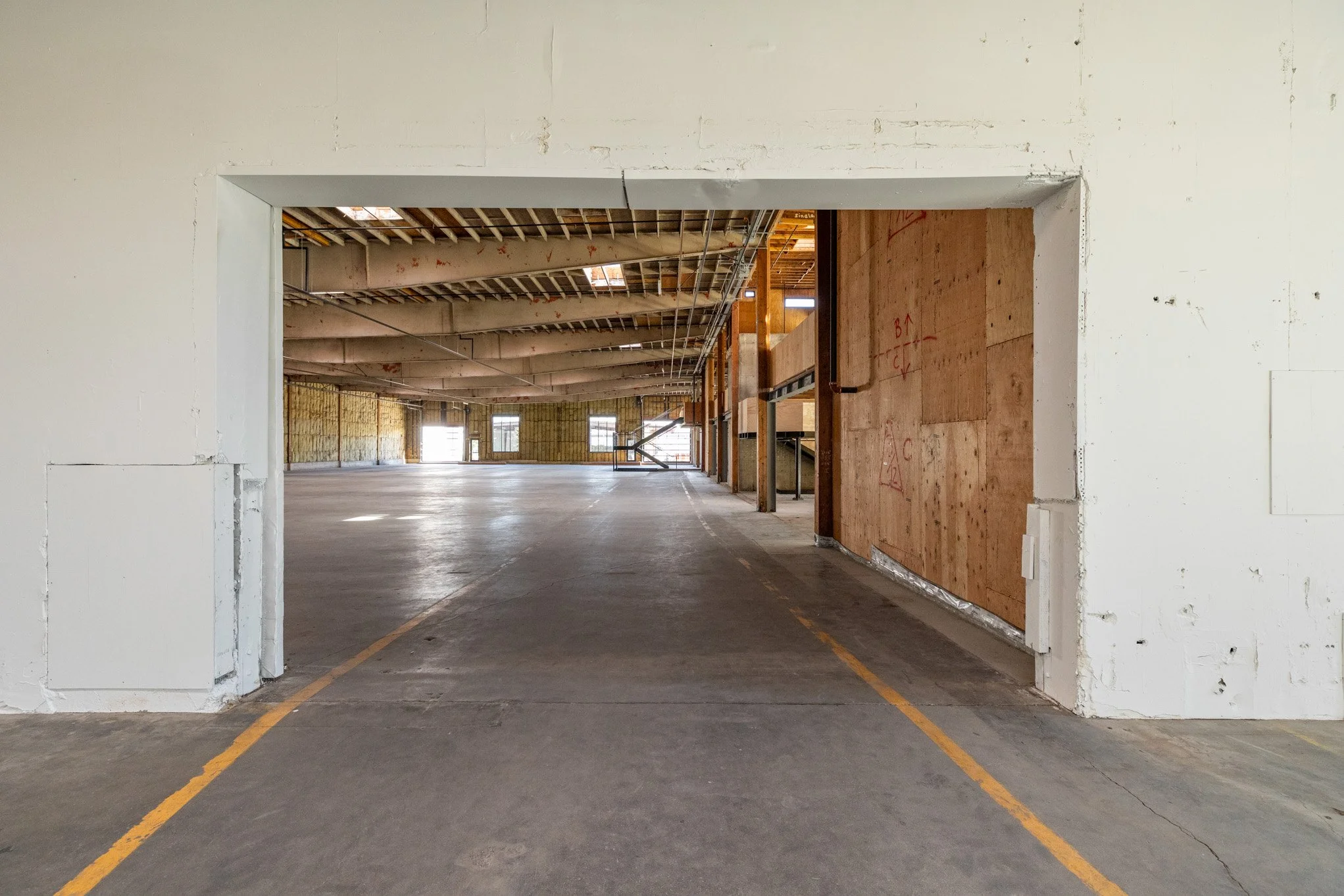 Empty parking garage with unfinished walls and ceiling, visible wood framing, and yellow parking space lines on the floor.