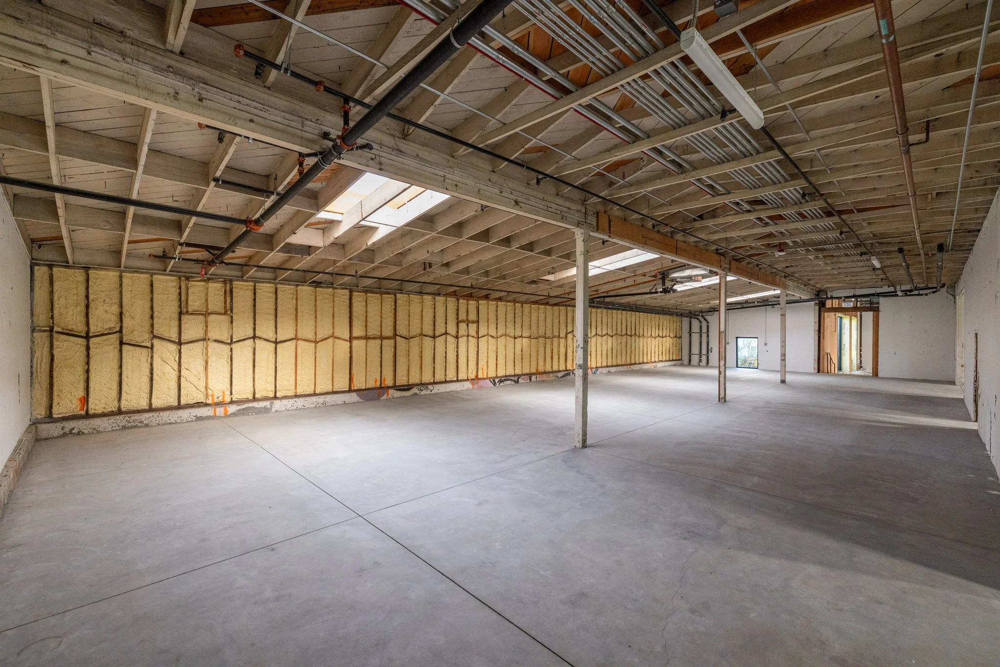 Empty attic space under construction with exposed roof framing, insulation, ventilation ducts, and concrete floor.