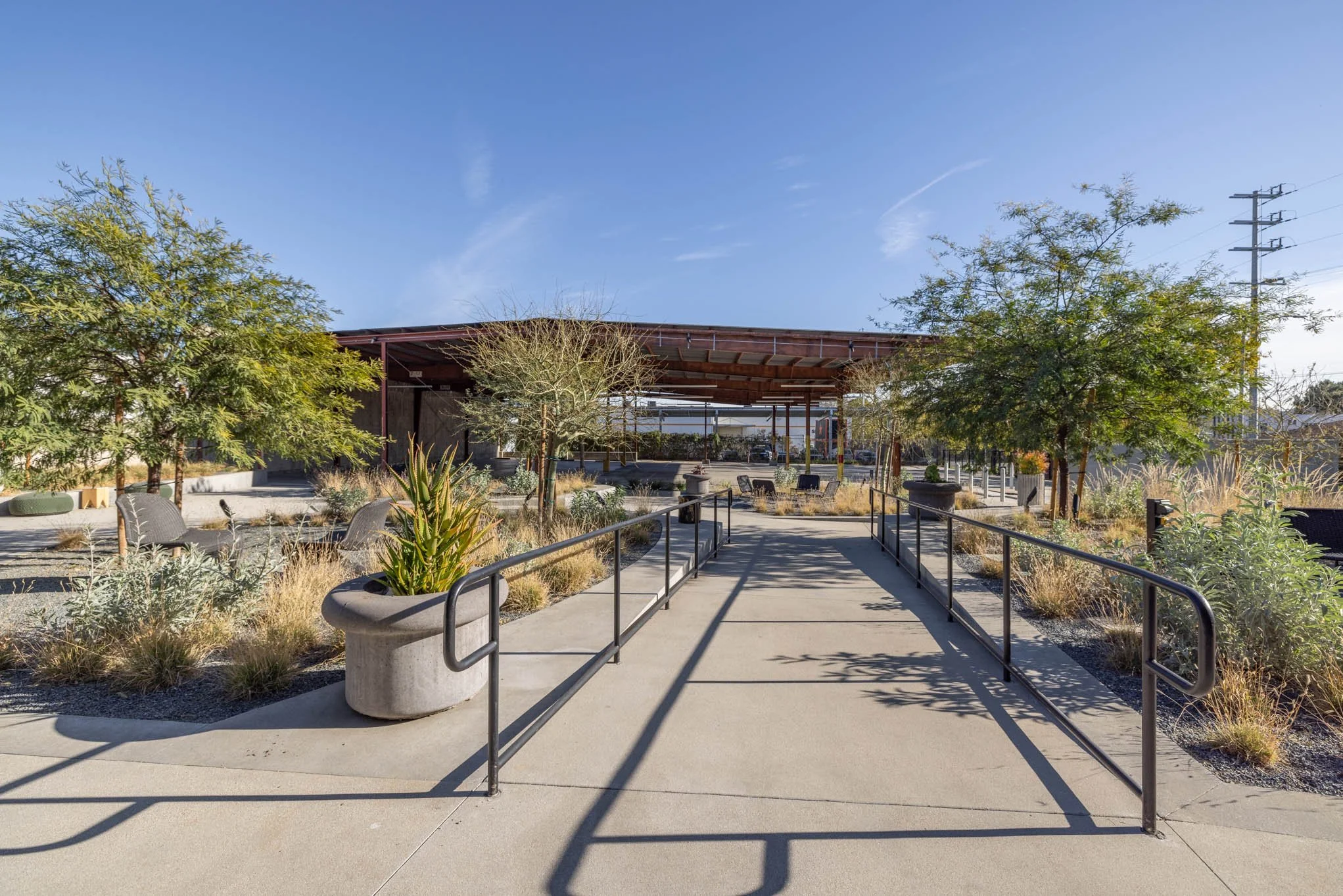 Outdoor park with pathway, benches, trees, and a wooden pavilion under a clear blue sky