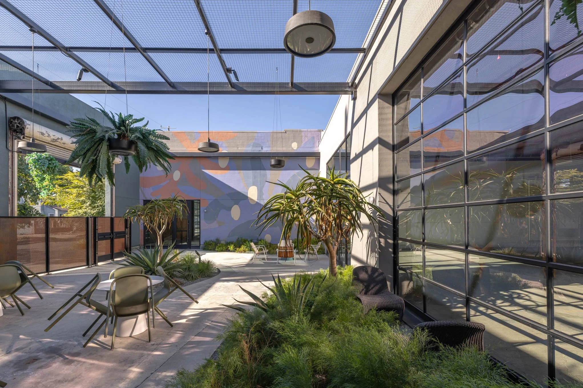 Indoor outdoor patio with plants, glass windows, and outdoor chairs under a metal pergola