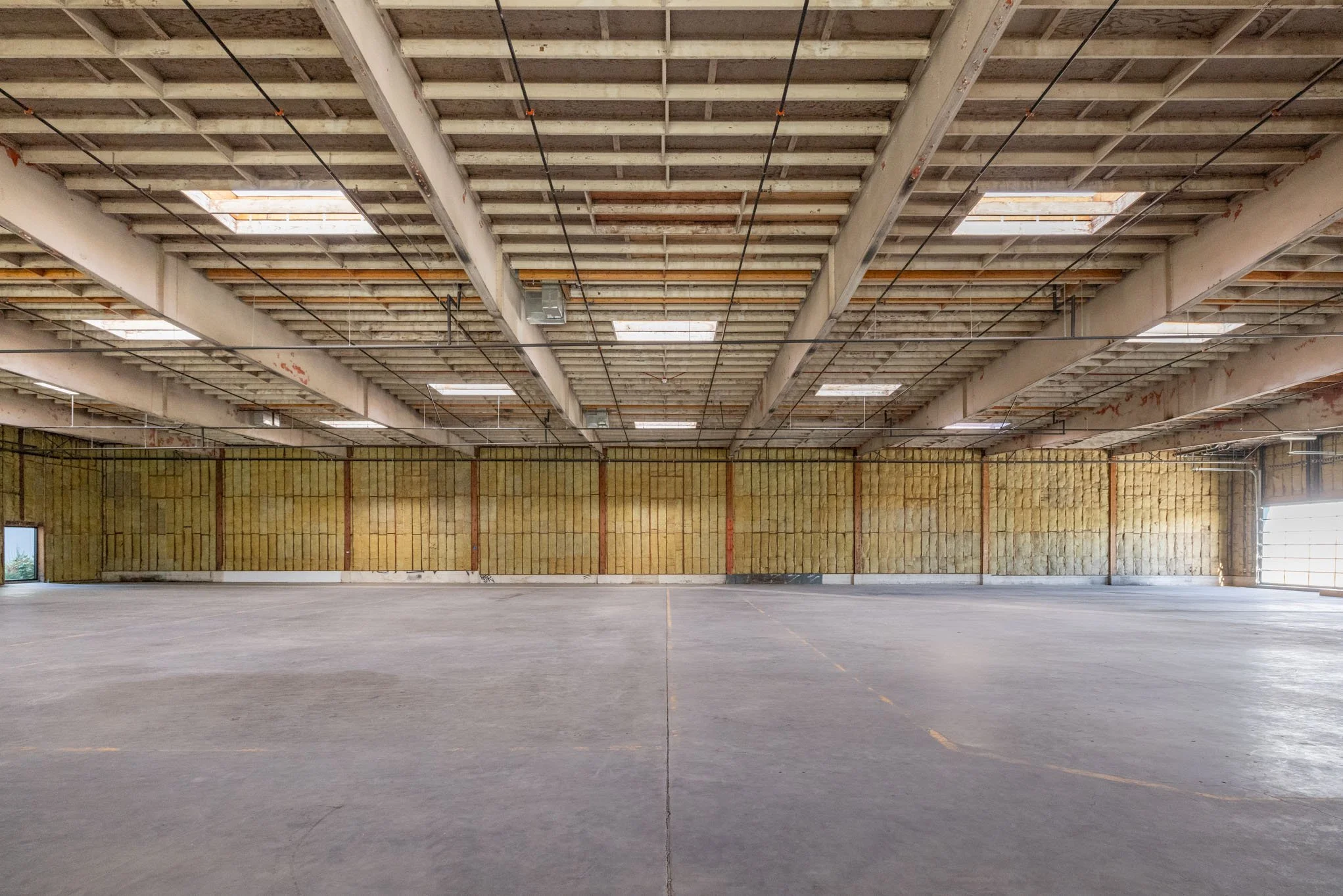 Empty warehouse with unfinished walls and exposed ceiling rafters.