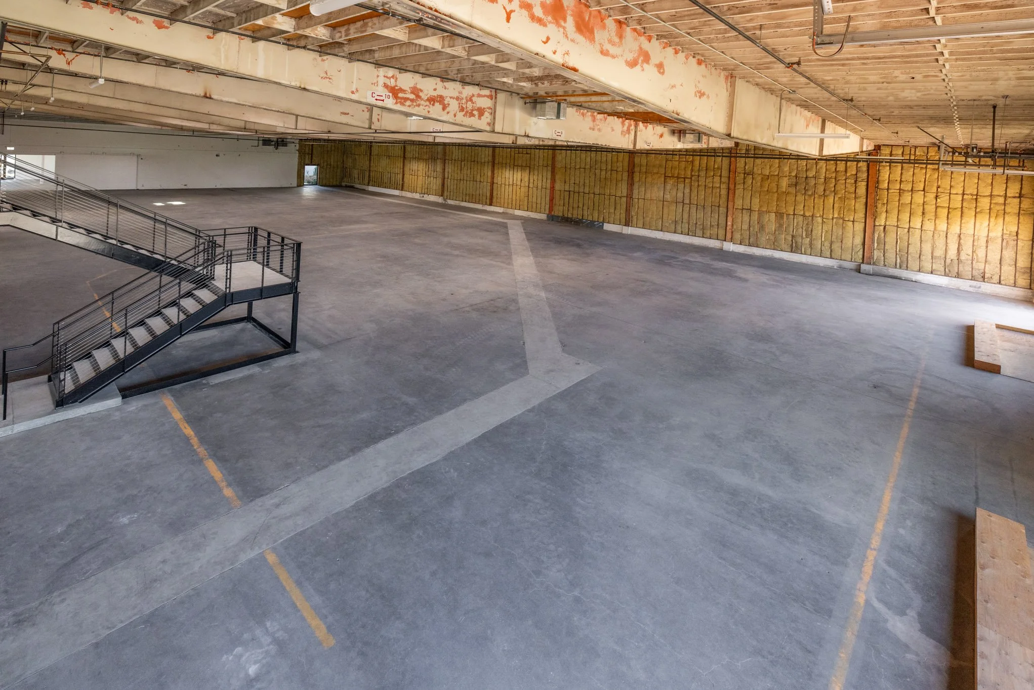 Empty indoor parking garage with concrete floor, yellow parking lines, a metal staircase, and unfinished walls.