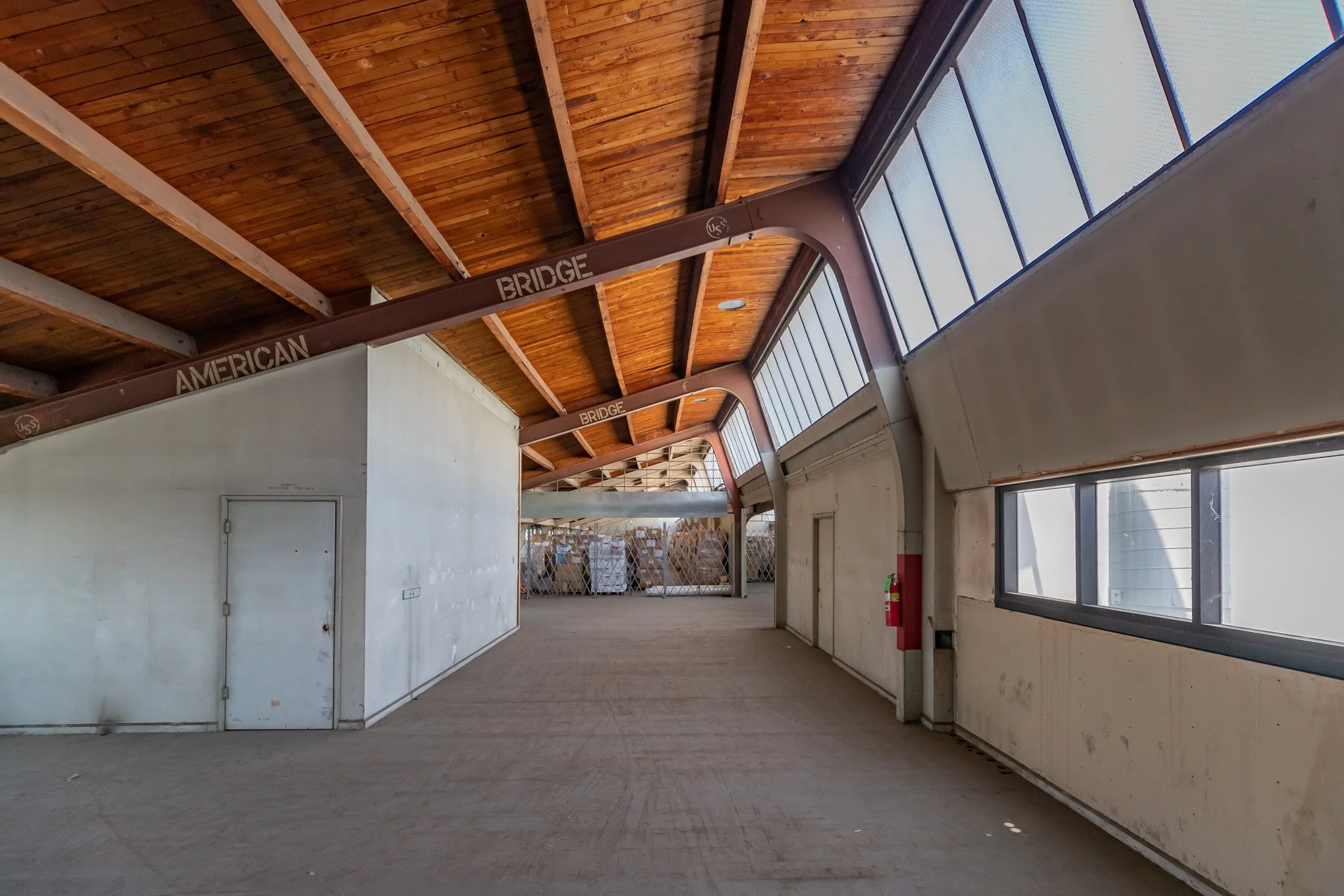 Indoor space with a wooden ceiling, a fire extinguisher on the wall, large windows, and a metal bridge labeled 'American Bridge'.