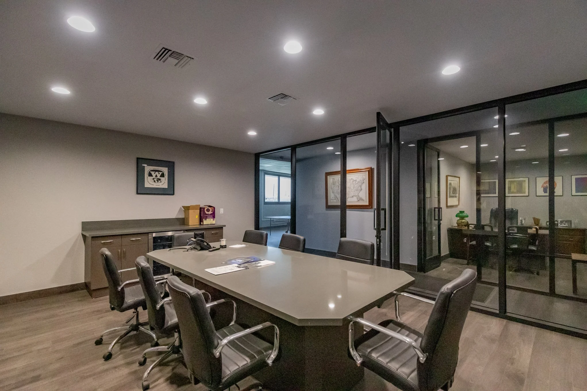 Empty conference room with a large oval table, black chairs, glass walls, and framed artwork.