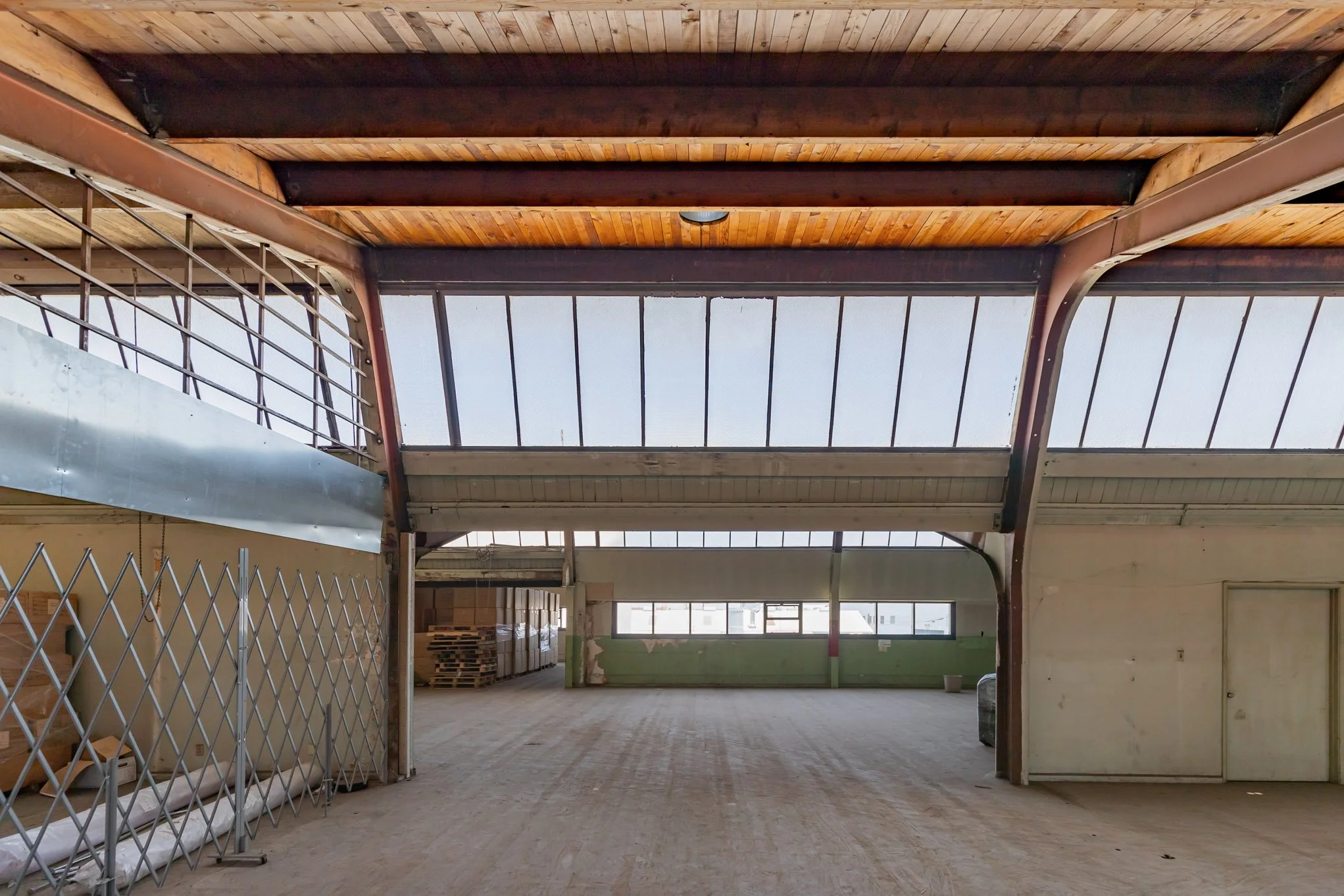 Empty industrial warehouse with large windows, wooden ceiling, and metal framing.