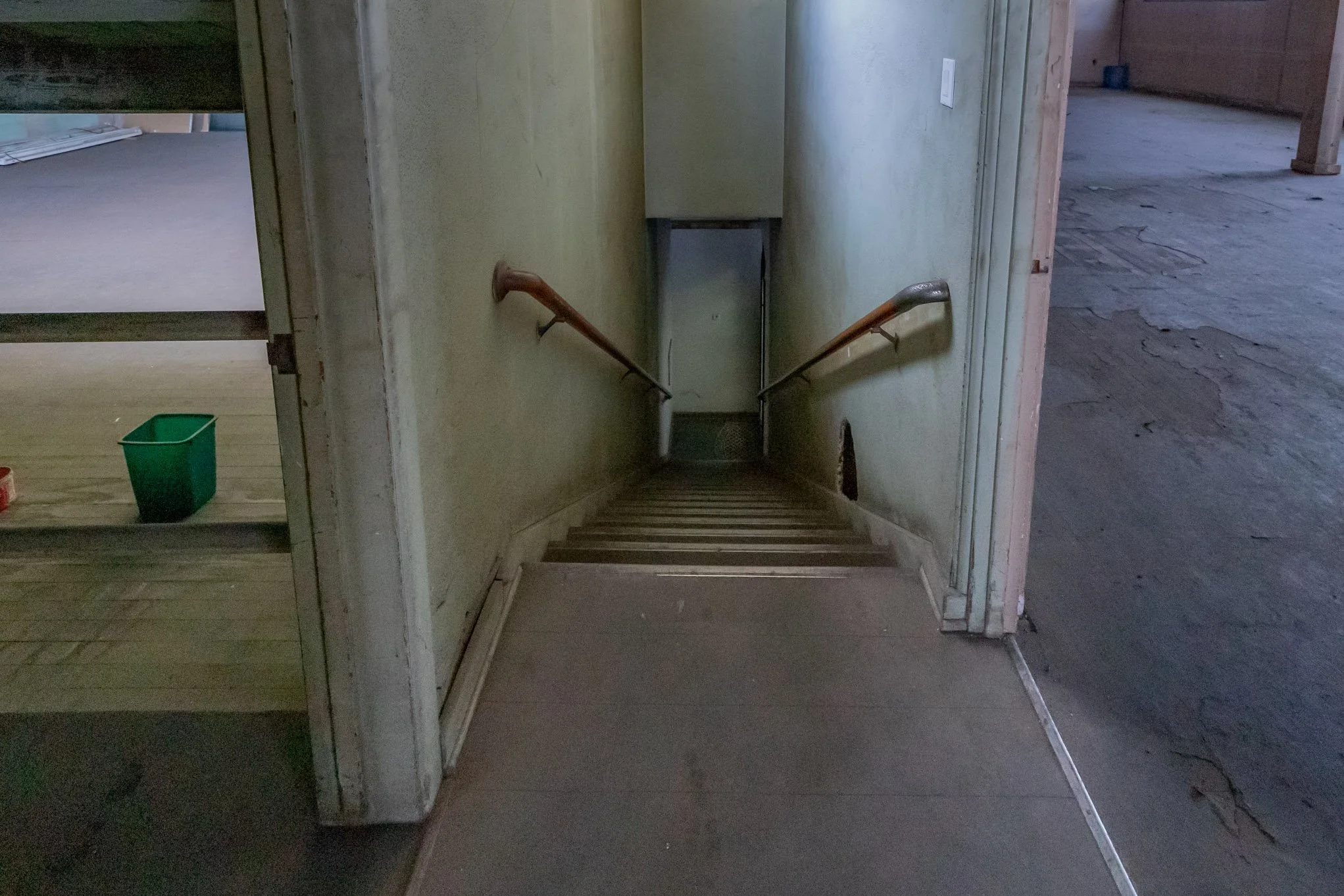 Photo of a staircase descending into a dark basement or cellar, with wooden handrails on both sides and a small door at the bottom.