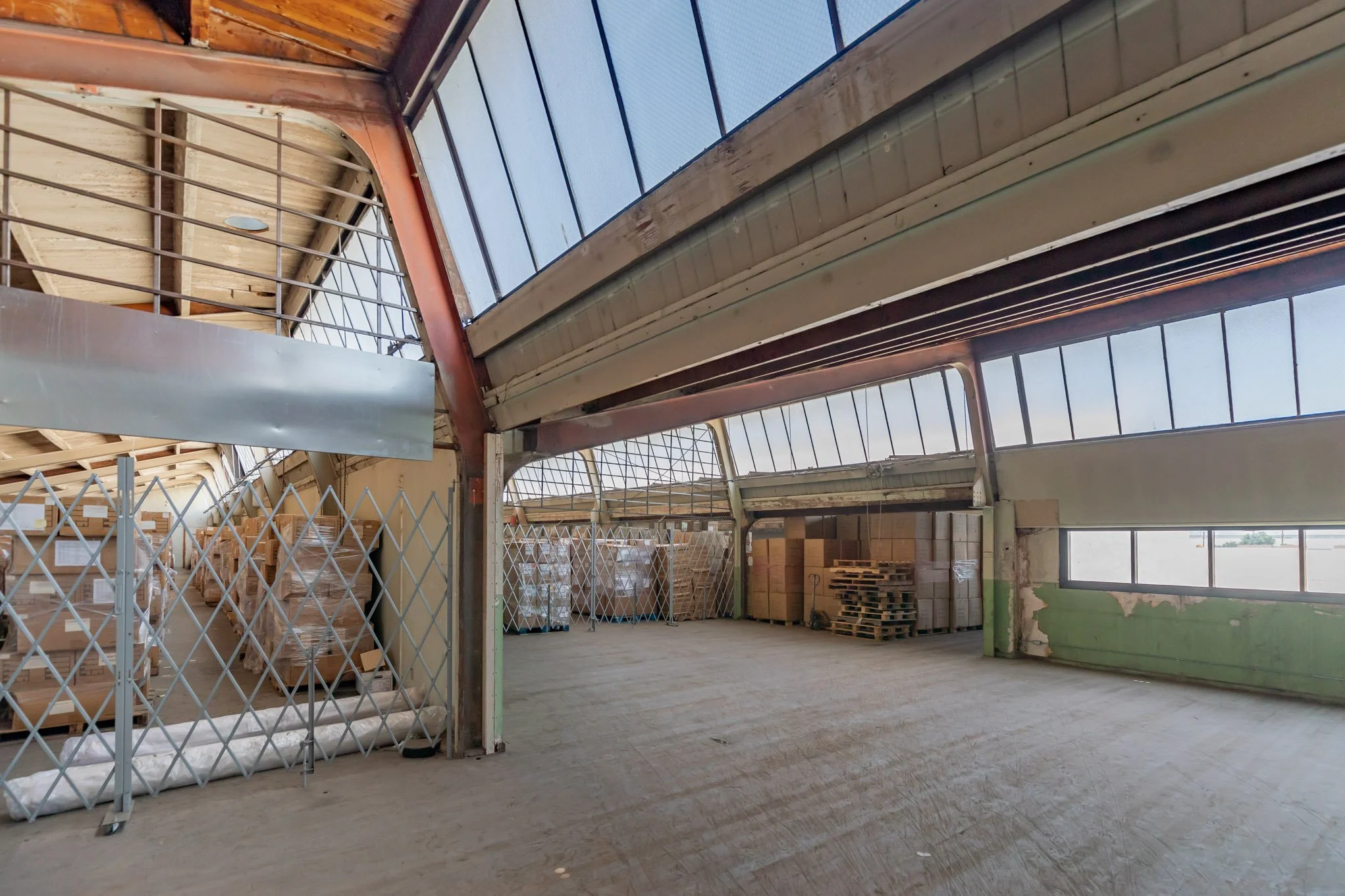 Empty warehouse with high ceiling, large windows, and stacked pallets of boxes.