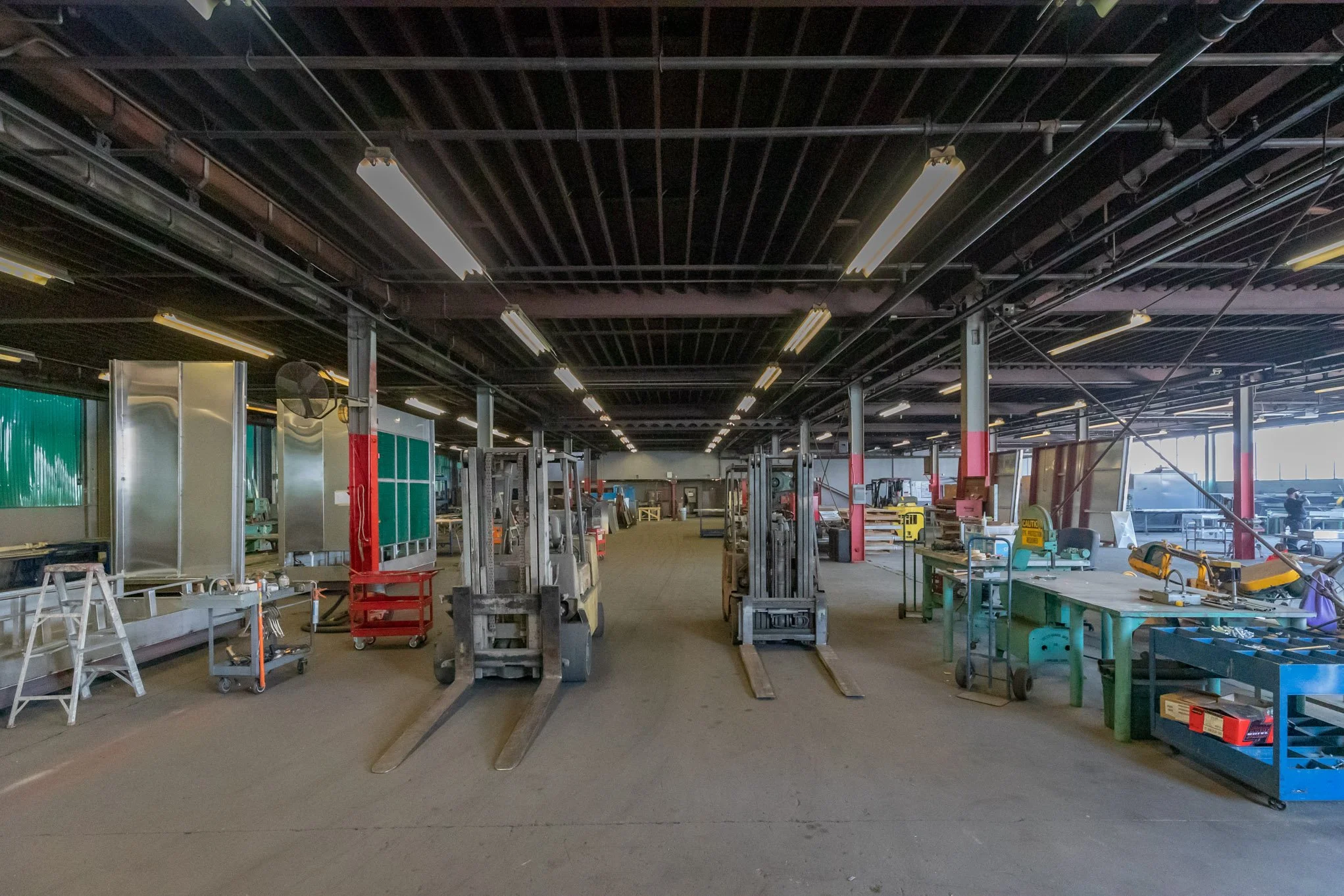 Empty industrial warehouse with forklifts, workbenches, and equipment for manufacturing or woodworking.