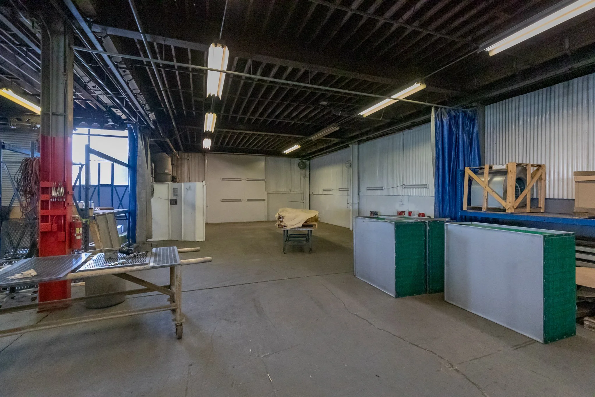 Empty workshop or industrial space with metal walls, concrete floor, and various tools and equipment stored along walls.