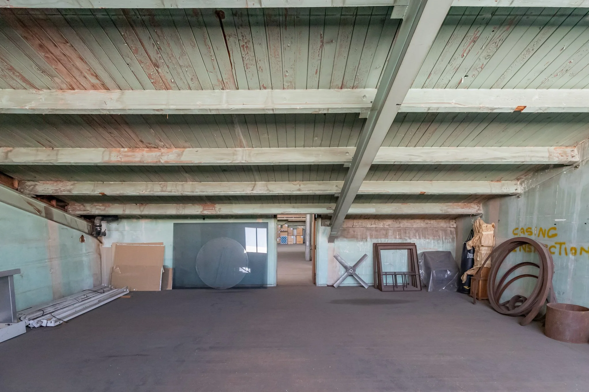 Empty attic with wooden ceiling beams and various stored items including frames, a fan, and coiled hoses.