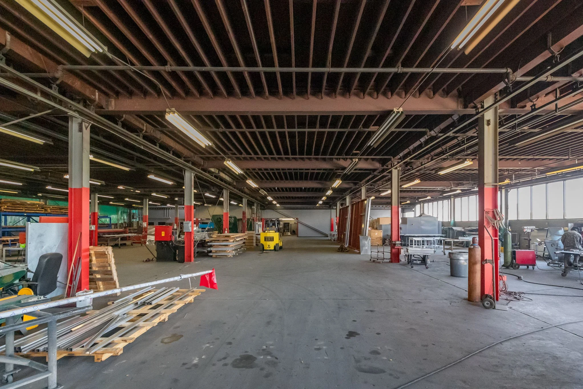 Interior of a large industrial warehouse with various equipment, pallets, and workers in the background.