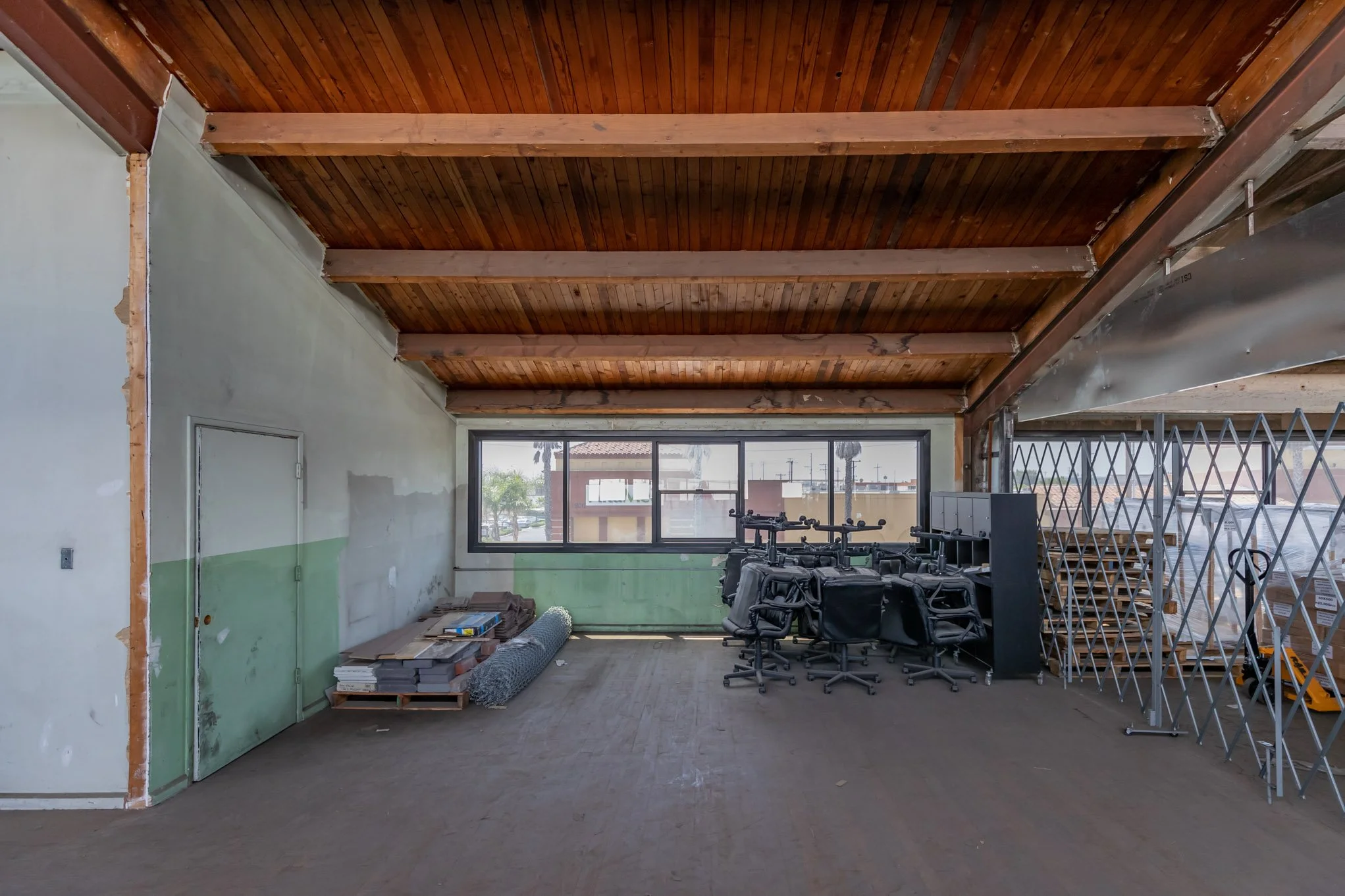 Interior of a partly renovated room with unfinished walls, stacks of construction materials, office chairs, and metal scaffolding.