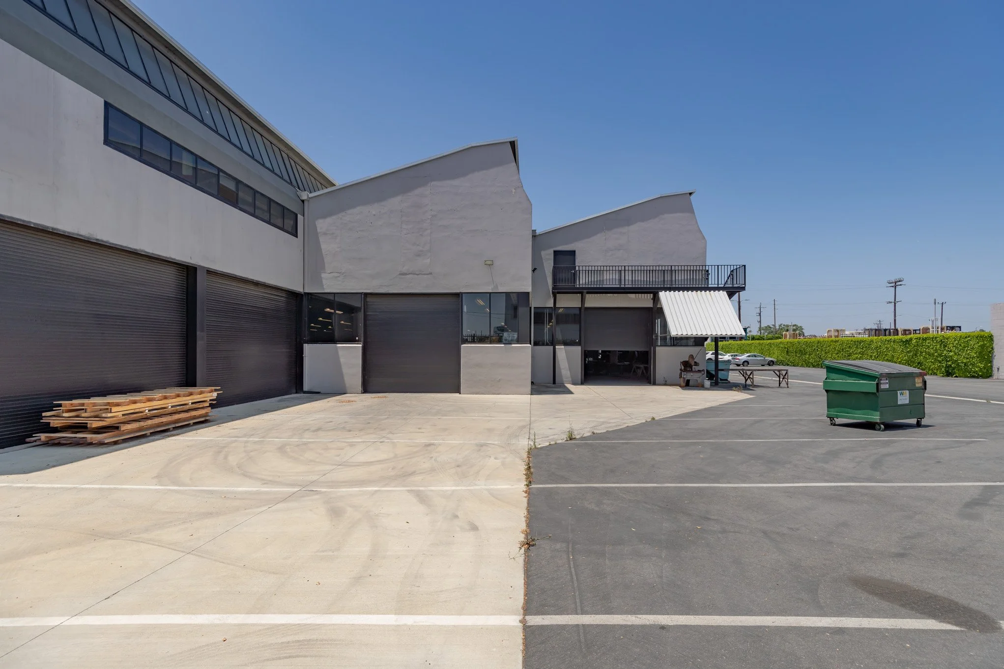 Empty parking lot with a building, some furniture, and a green dumpster, under a clear blue sky.