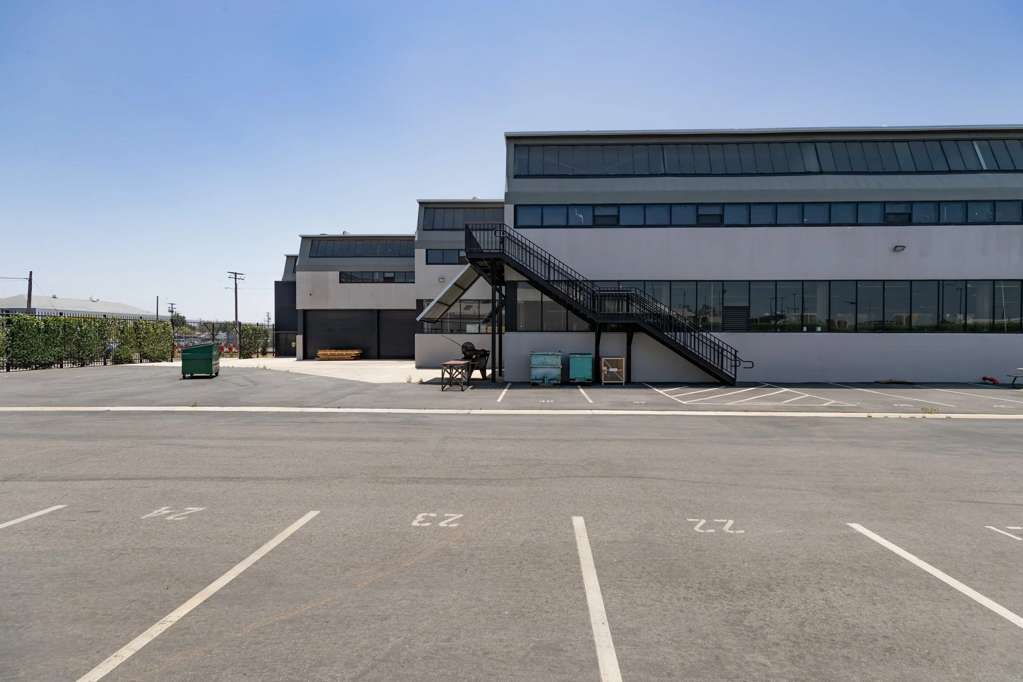 Empty parking lot in front of a modern industrial building with stairs and large windows.
