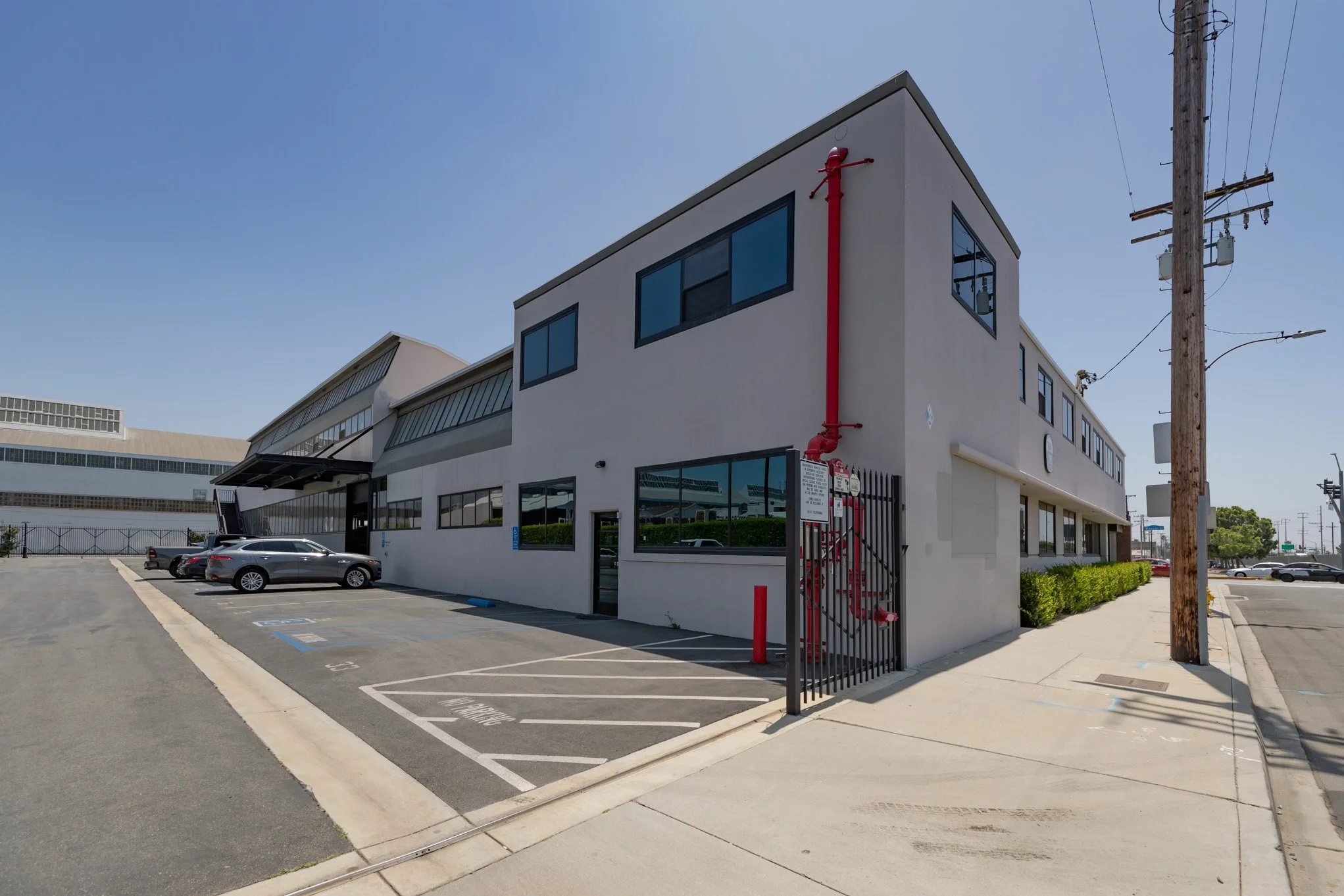 Empty parking lot next to a modern white building with large windows and a red fire alarm pipe