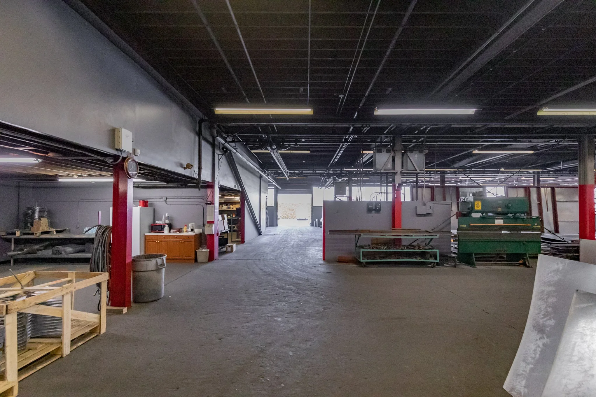 Interior of an unfinished commercial or industrial space with construction tools, equipment, and workbenches, illuminated by natural light from an open door at the back.