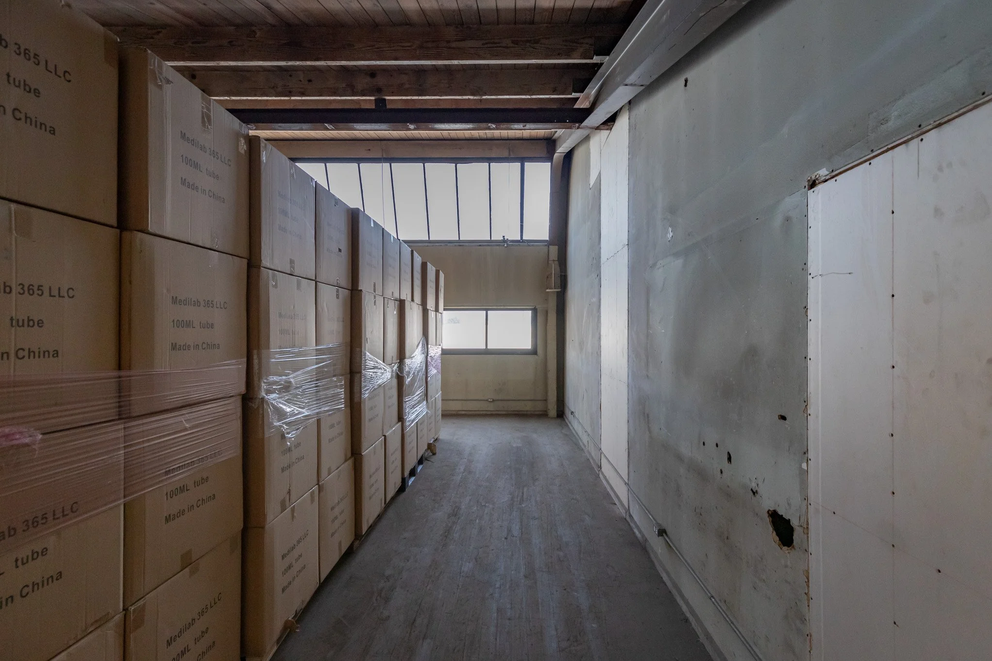 Warehouse with stacked cardboard boxes on the left and a window at the end of the room.