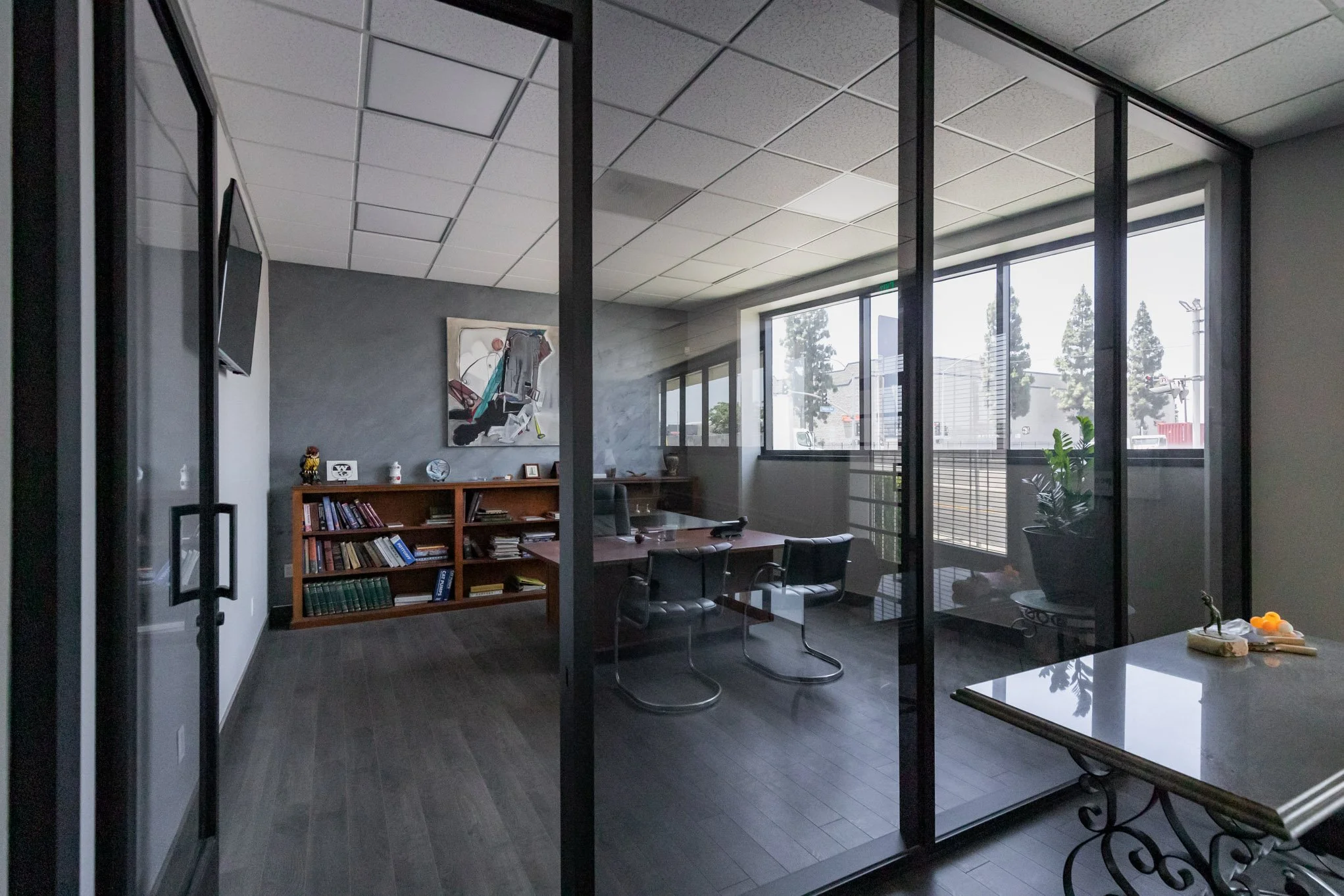 Empty office with wood floor, glass wall, desk, and chairs.