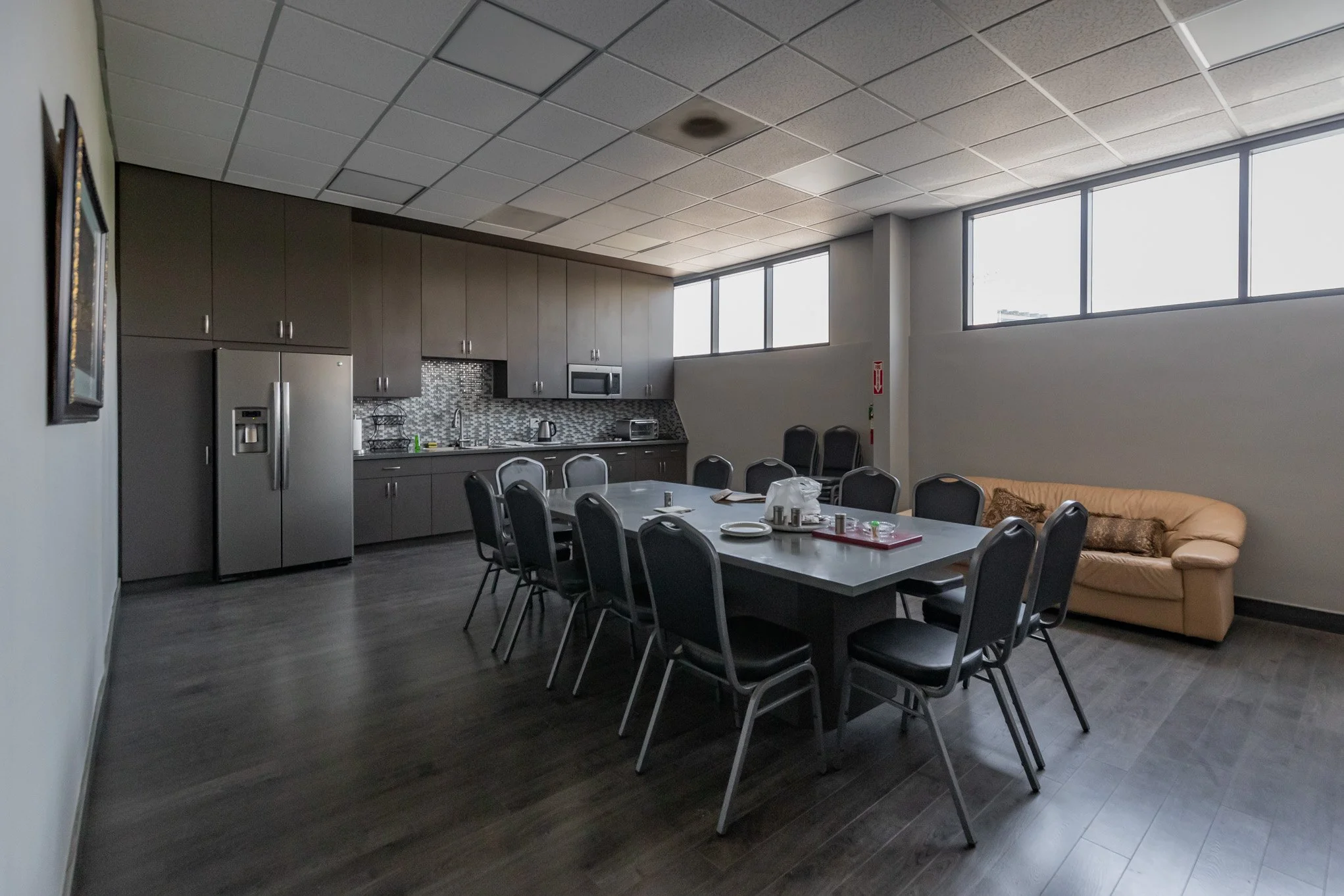Empty conference room with a long table, chairs, kitchenette, and a beige couch near the windows.