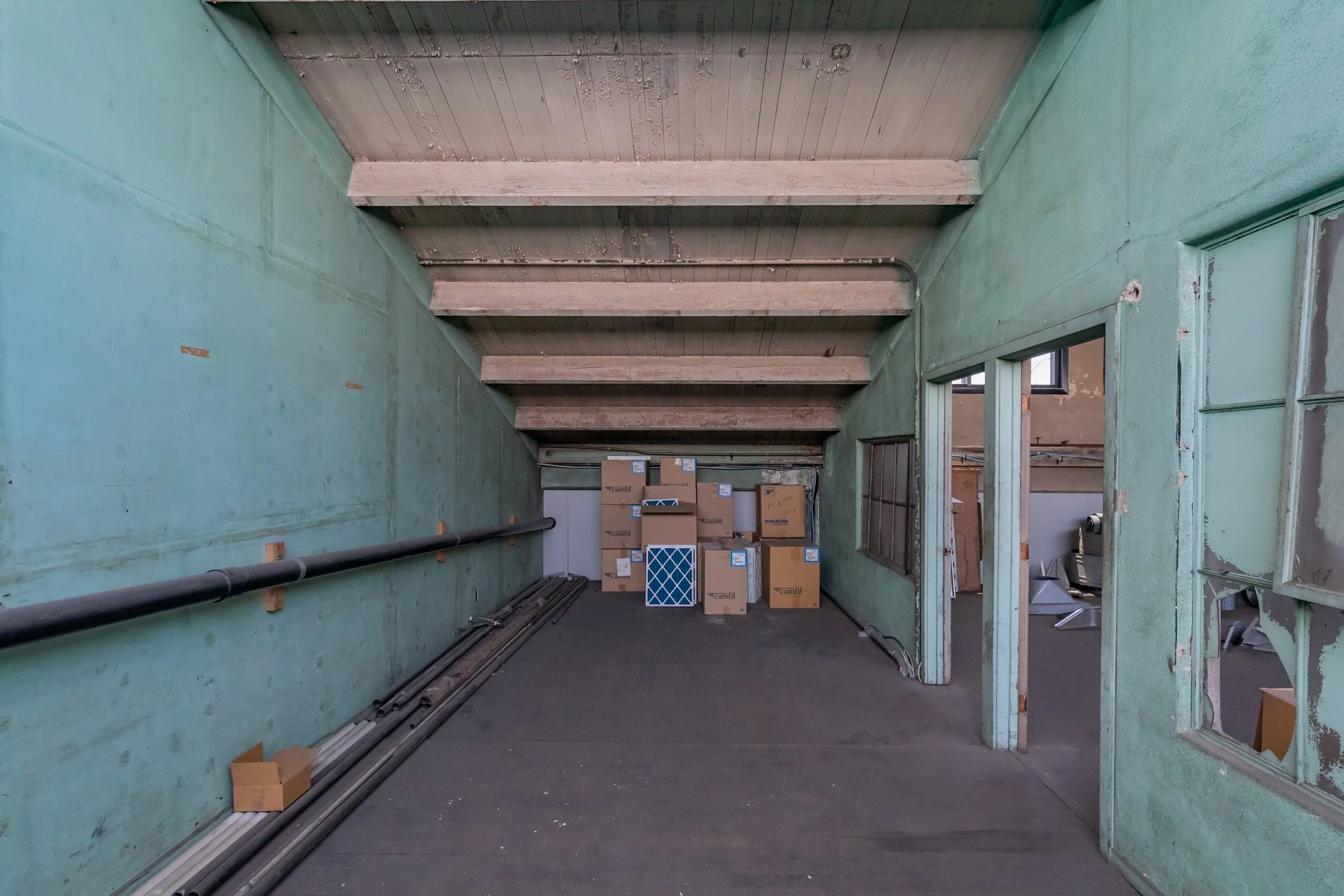 Empty room with green painted walls, wooden ceiling beams, and boxes stacked in the corner, viewed through a doorway.