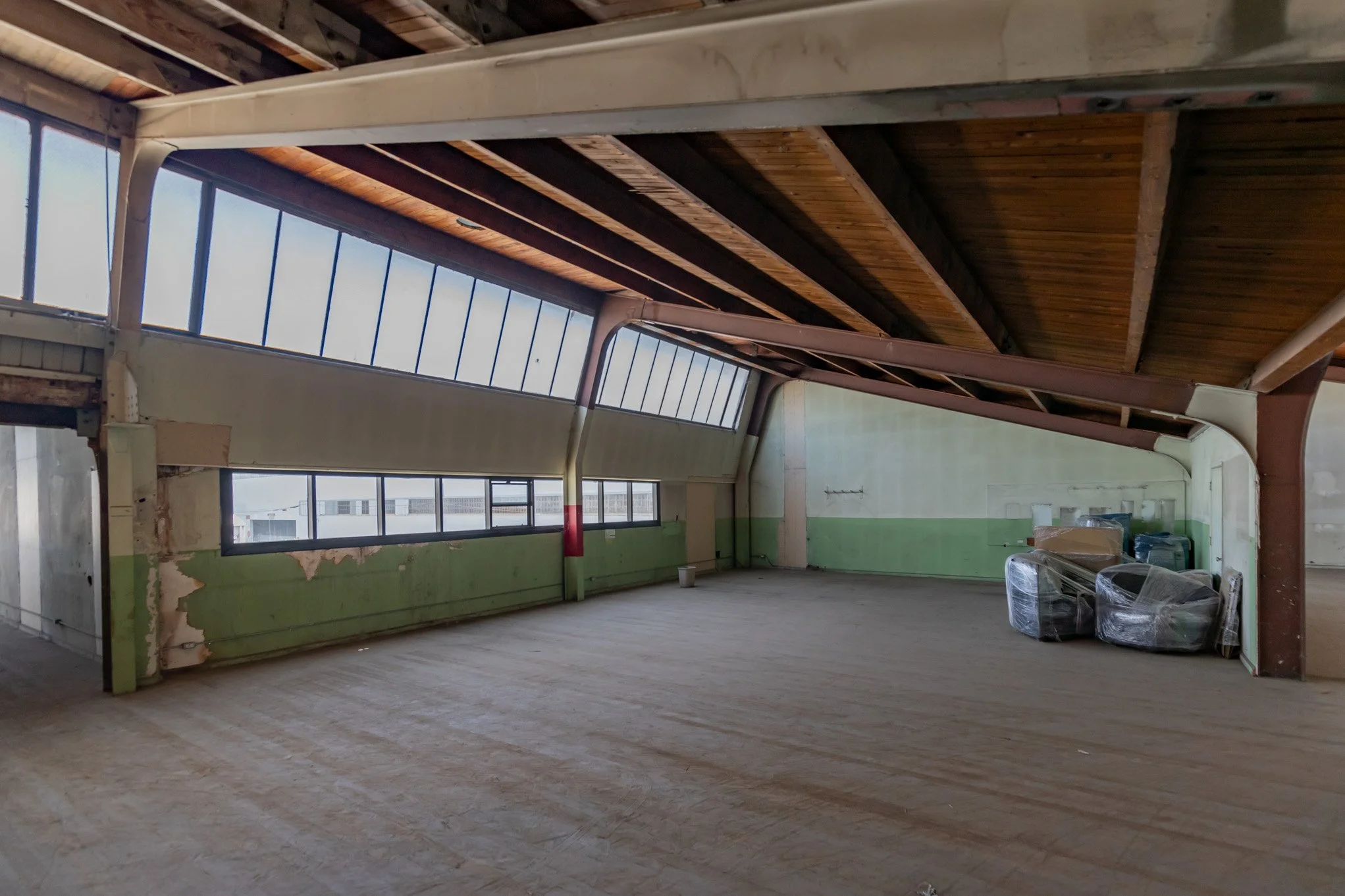 Empty indoor space with large windows, unfinished walls, and a wooden ceiling, possibly an attic or loft renovation site.
