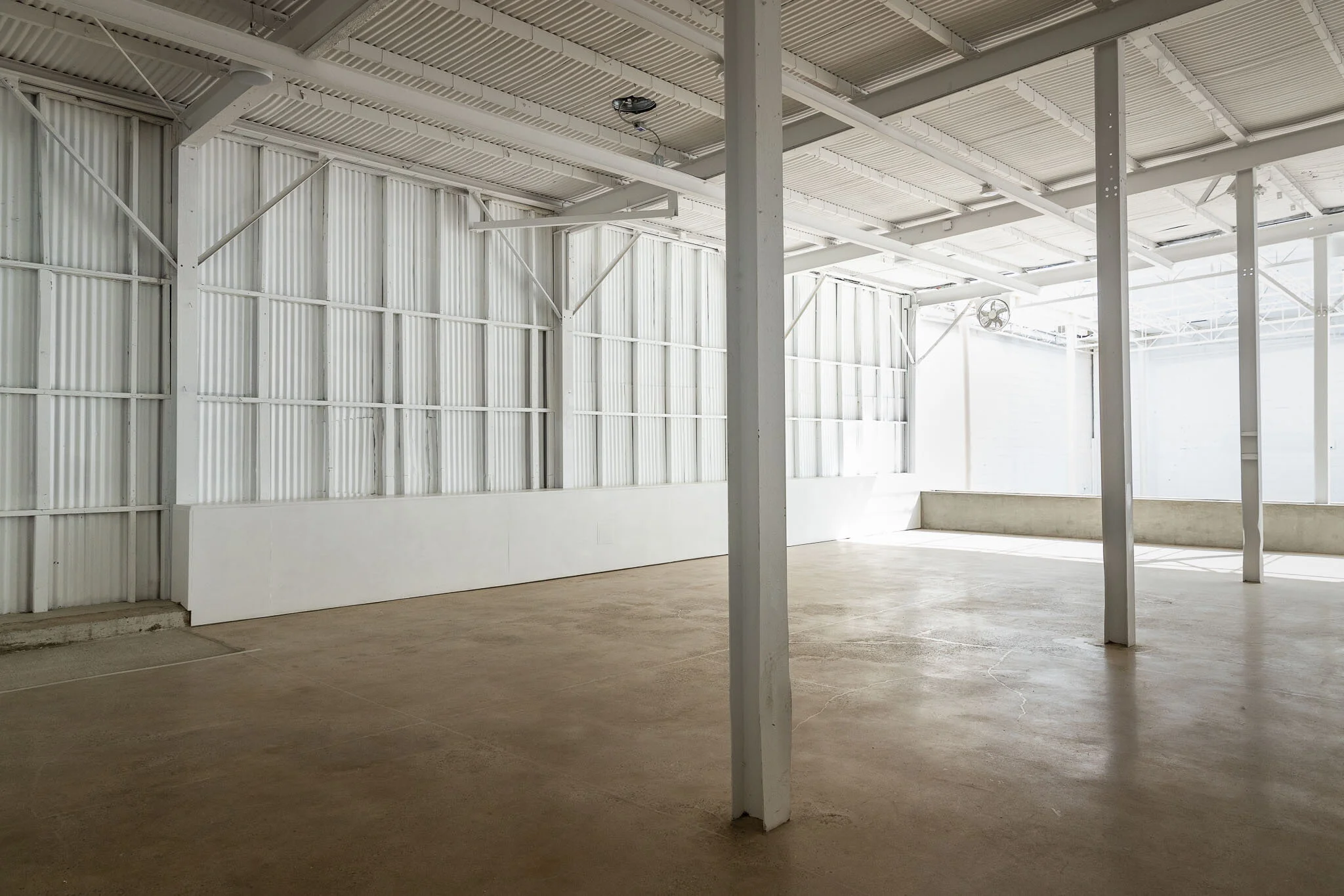 Empty indoor skate rink with white walls, metal ceiling, and concrete floor.