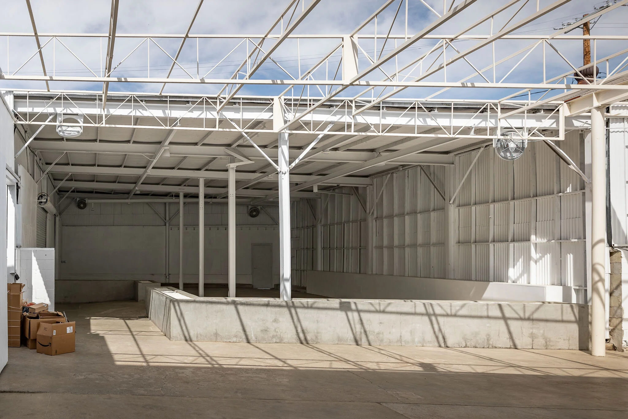 Empty industrial or warehouse space with white metal walls and roof, concrete support structures, and cardboard boxes on the left side.
