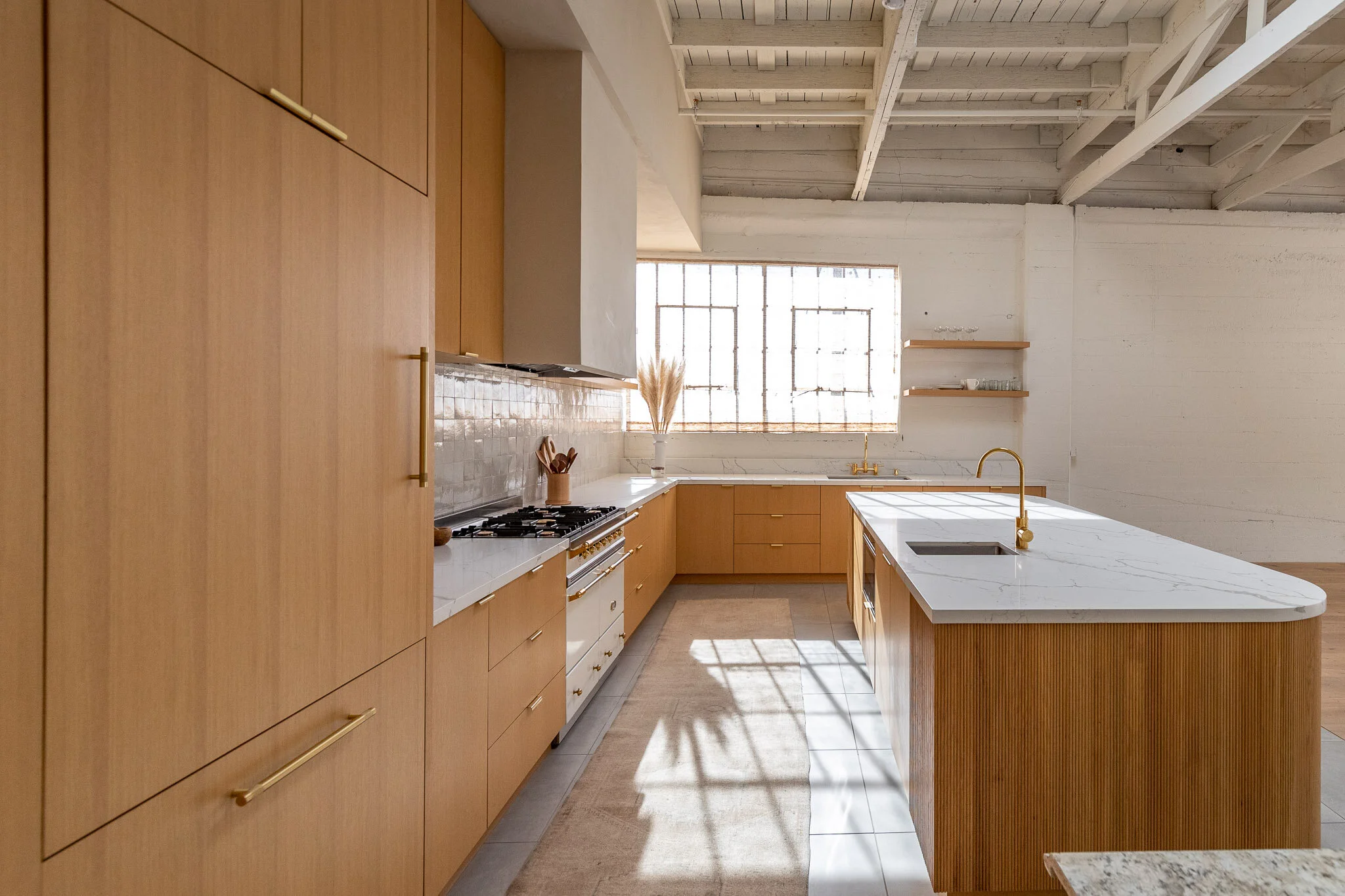 Modern kitchen with wooden cabinets, white marble countertops, a large island with a built-in sink, and a large window letting in natural light.