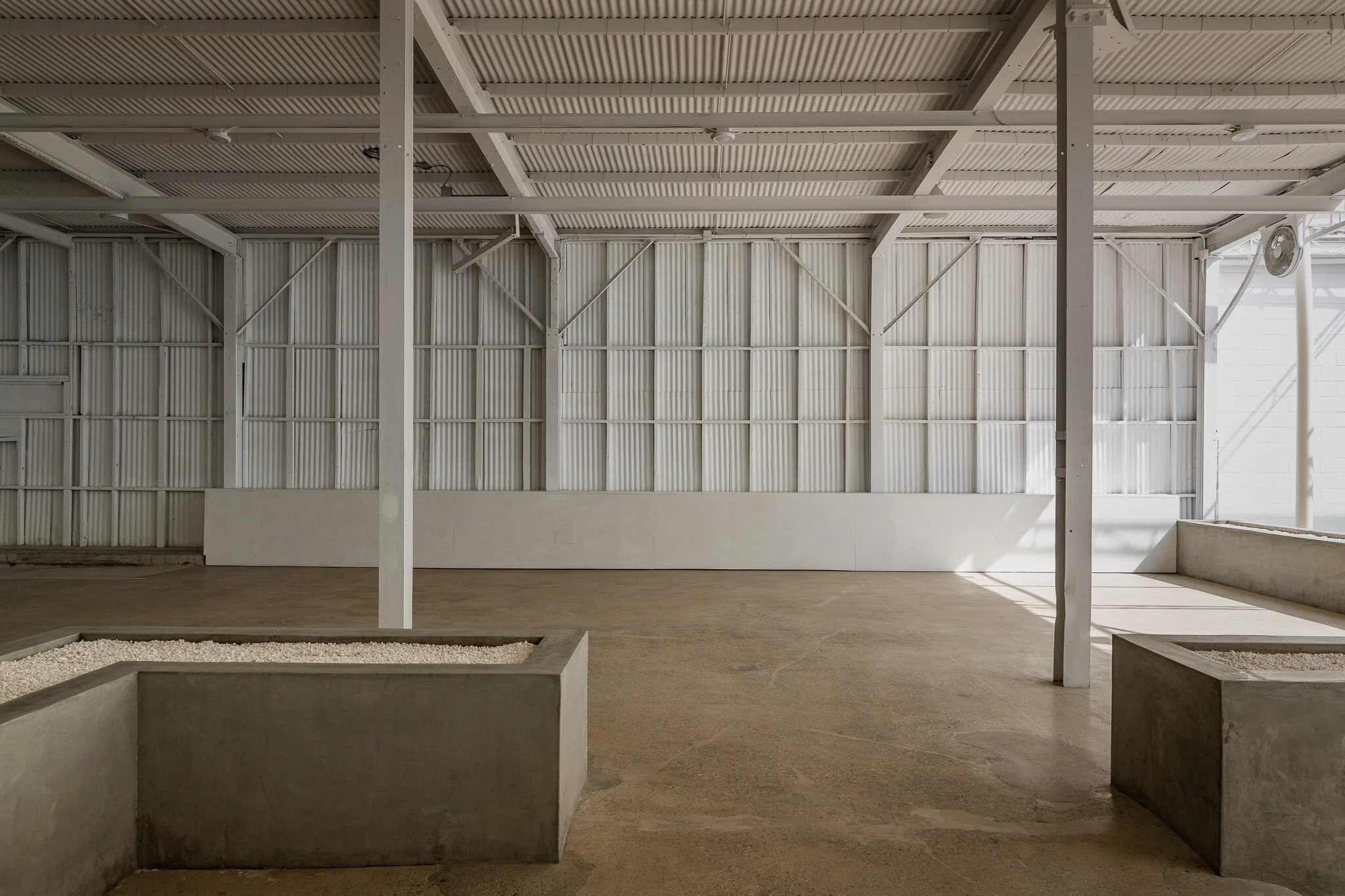 Empty indoor space with concrete planters and white metal walls and ceiling.