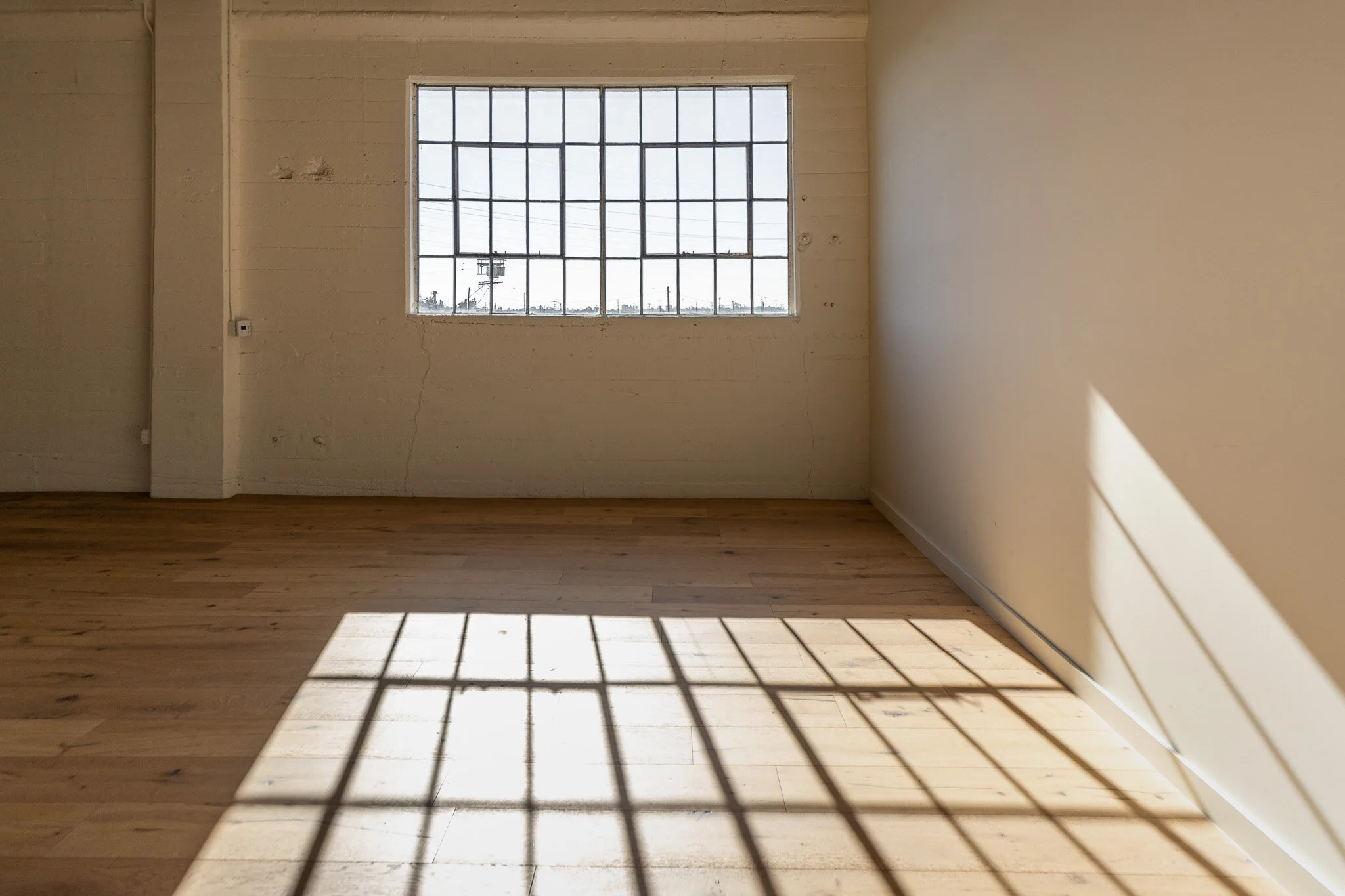 Empty room with a large window causing sunlight and shadow patterns on the hardwood floor.