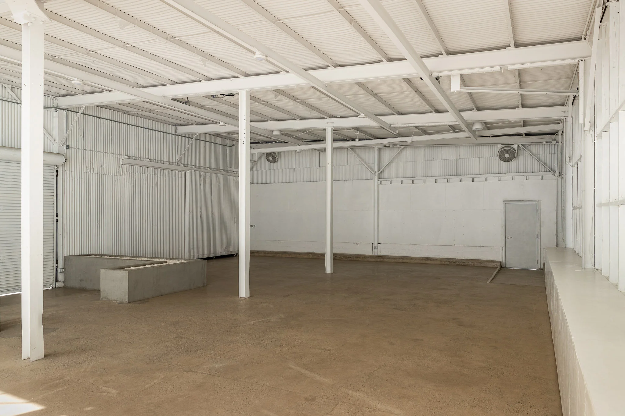 Empty industrial warehouse with white metal walls, a concrete block, and a dirt floor.