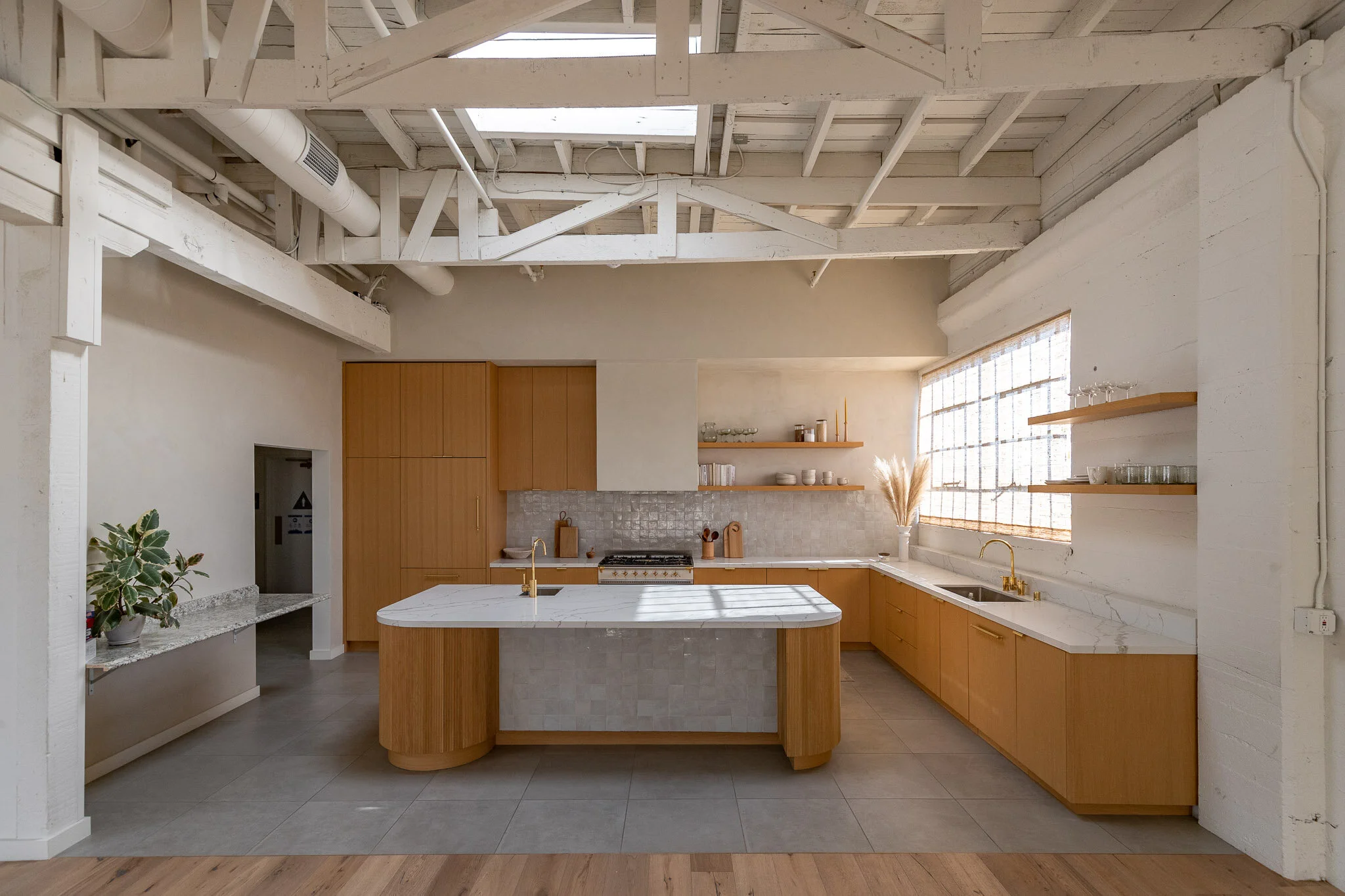 Modern kitchen with wooden cabinets, marble island, open shelving, large window, and exposed ceiling beams.