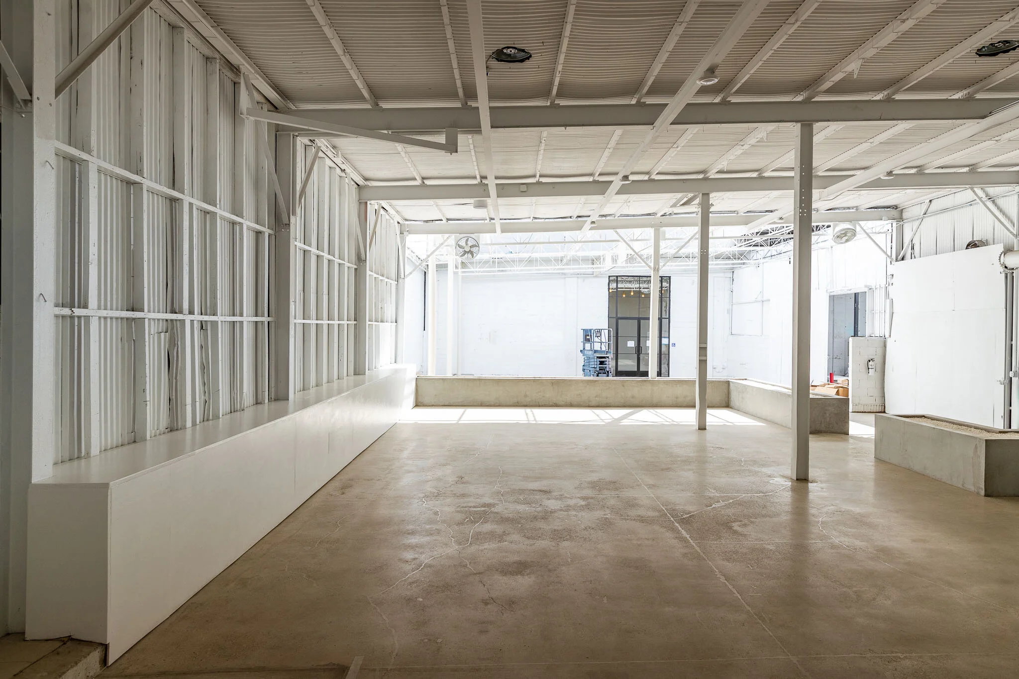 Empty indoor space with white walls and ceiling, concrete floor, and large open window at back letting in natural light.