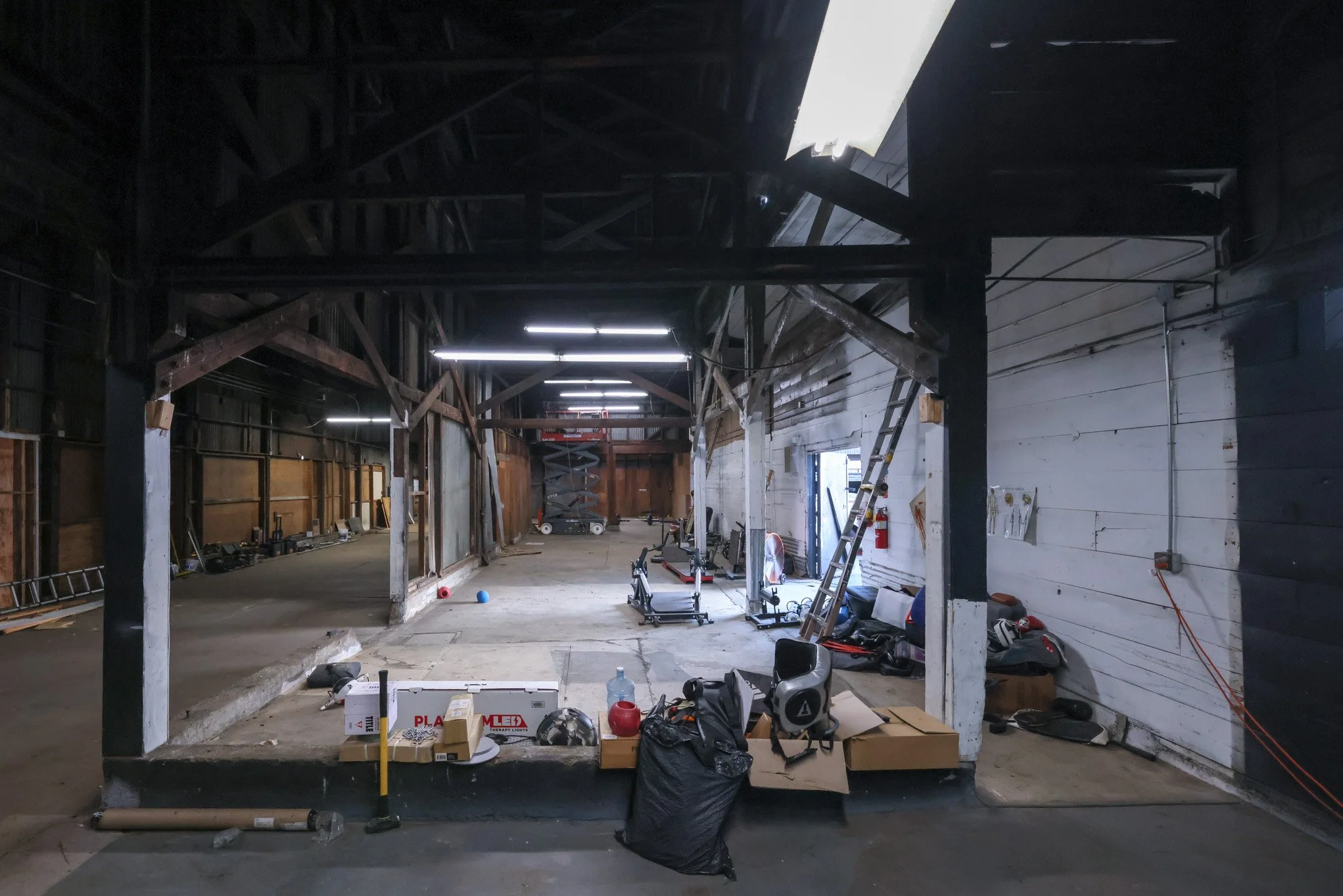 Interior of a construction site with wooden beams, unfinished walls, construction equipment, boxes, and ladders.