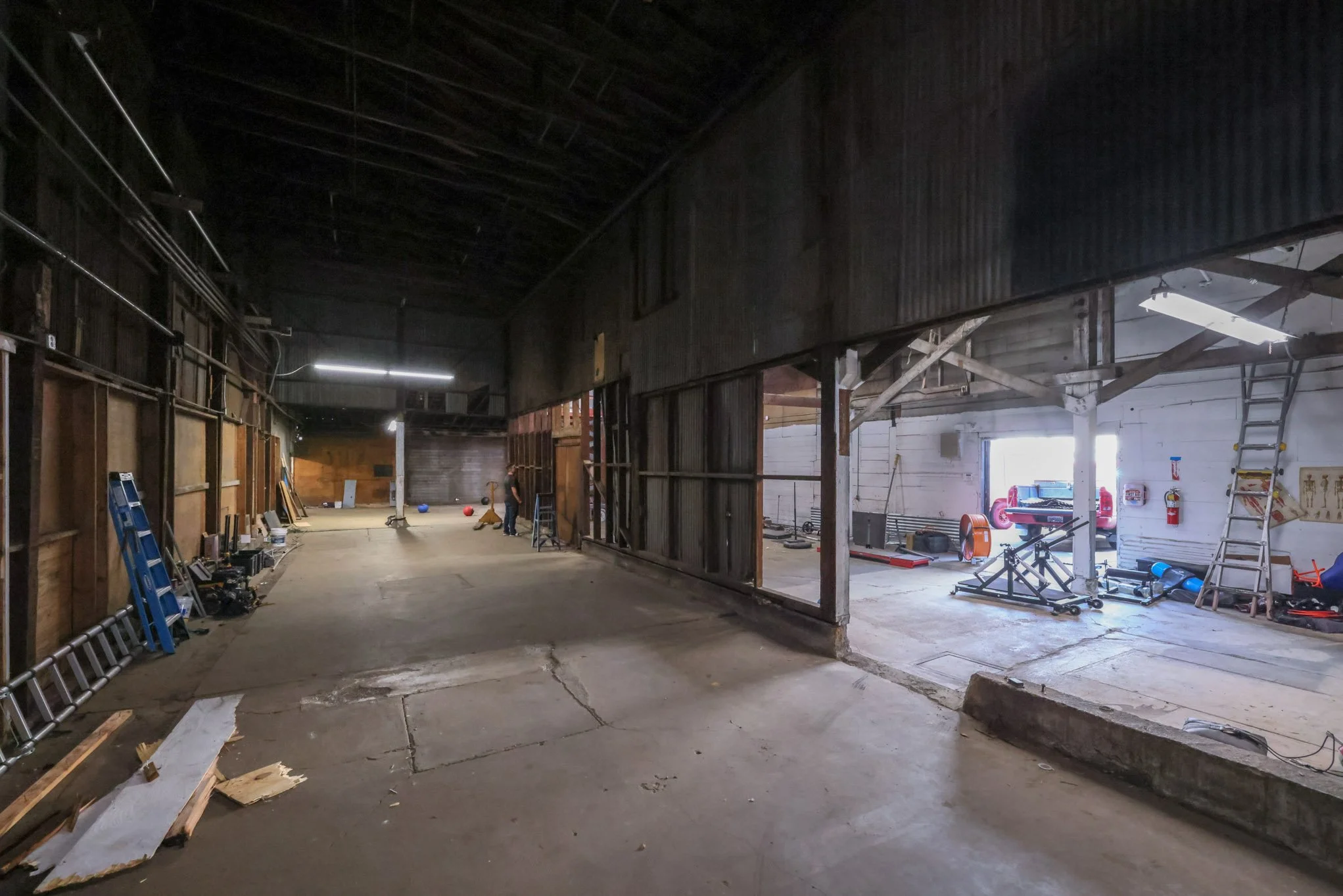 Interior of a partially renovated garage or workshop with tools, ladders, and equipment visible.