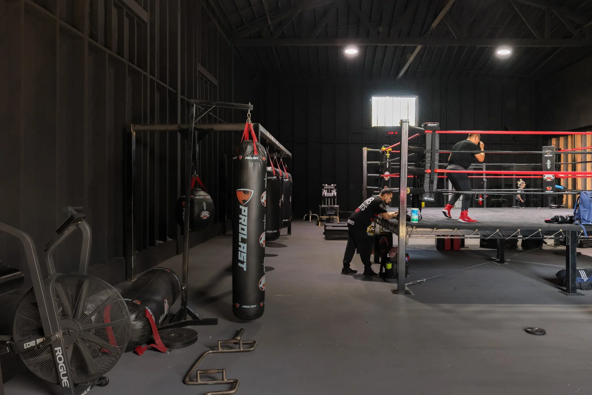 Boxing gym with punching bags, a boxing ring, and trainers preparing equipment.