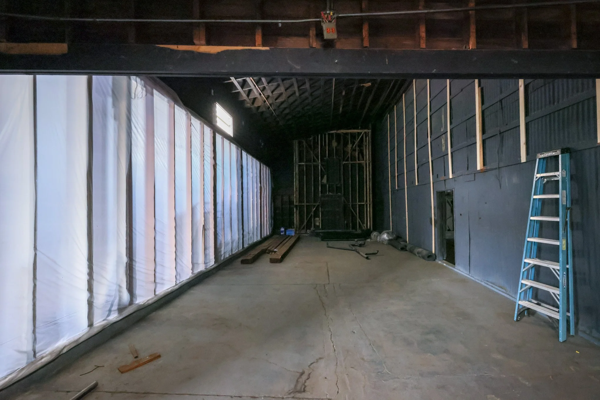 Interior of a room under construction with black walls, exposed framing, ladder, and scattered construction materials.