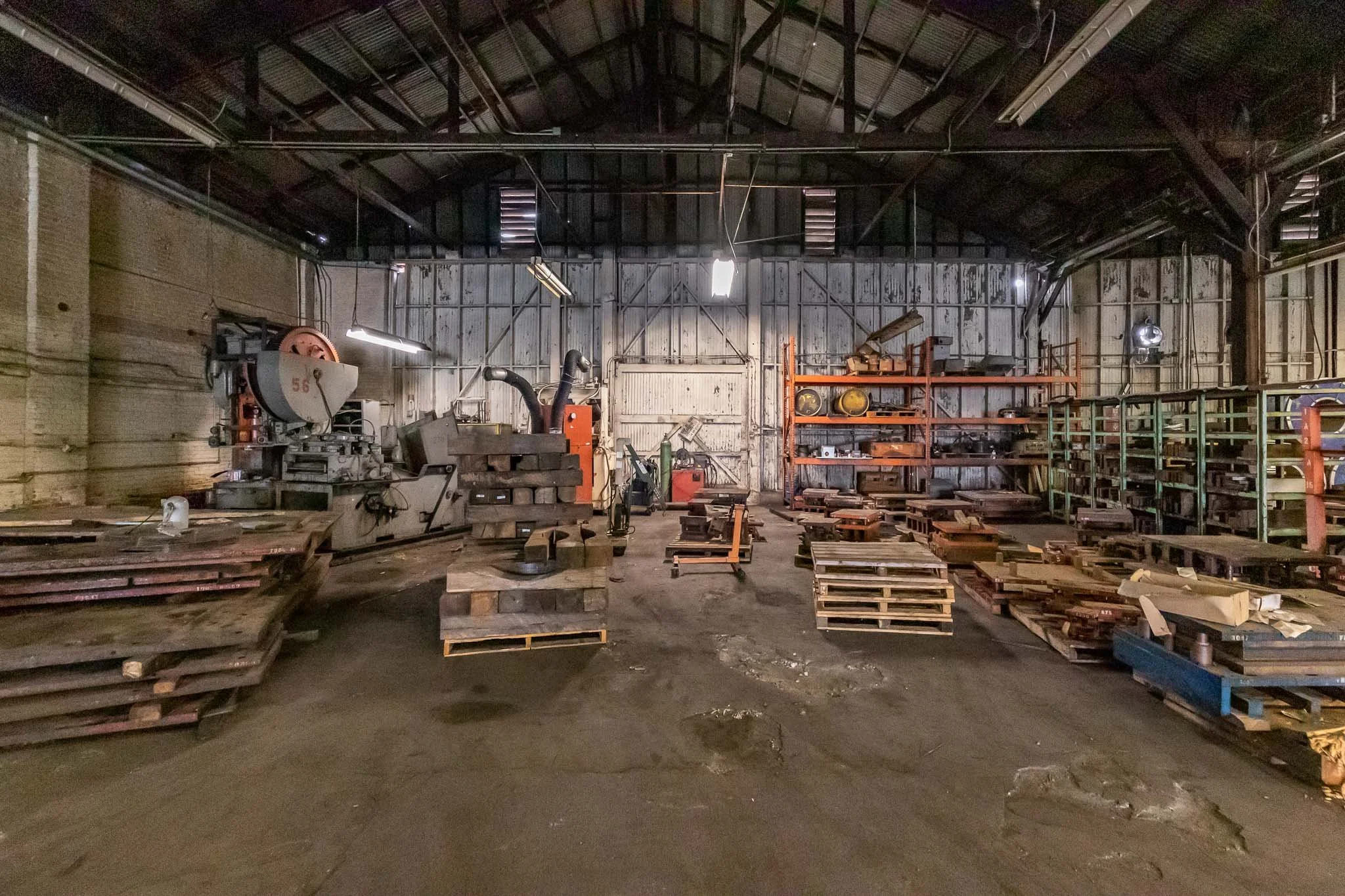 Empty industrial workshop with metal shelves, tools, and machinery, and a concrete floor.