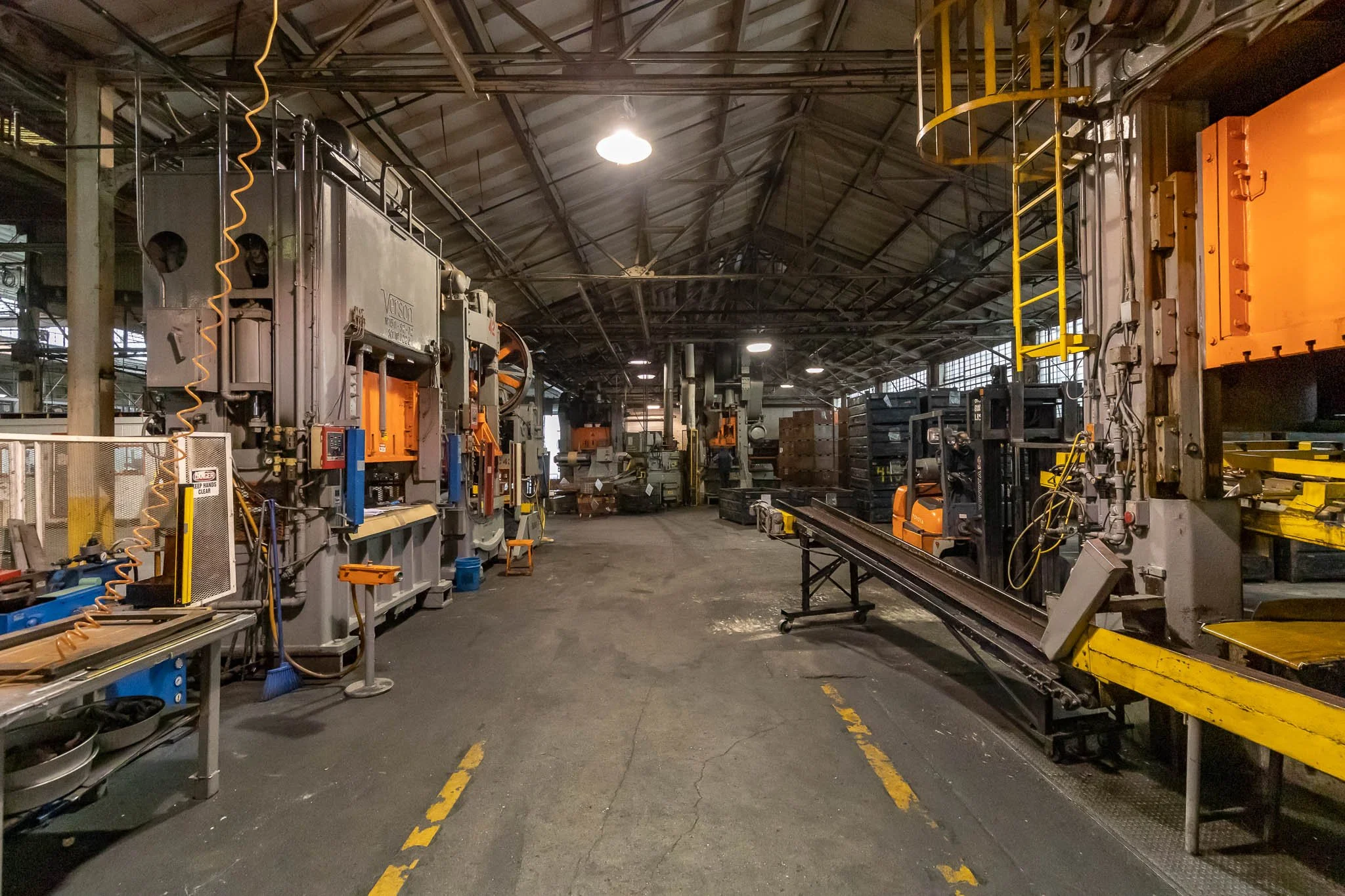 Inside an industrial manufacturing facility with large machinery, tools, and stacked pallets in a spacious warehouse.