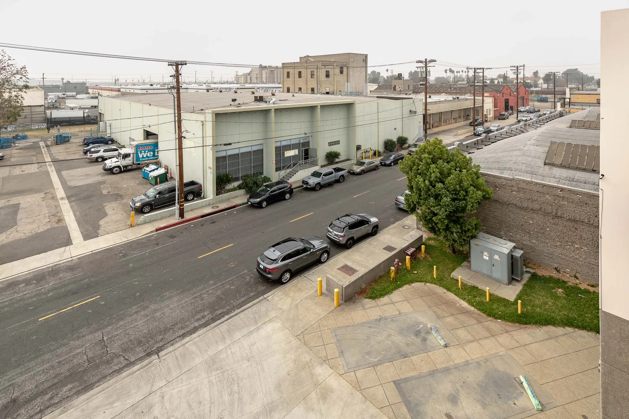 View of a city street with parked cars, a building with a Costco sign, an alley, and a tree near a sidewalk