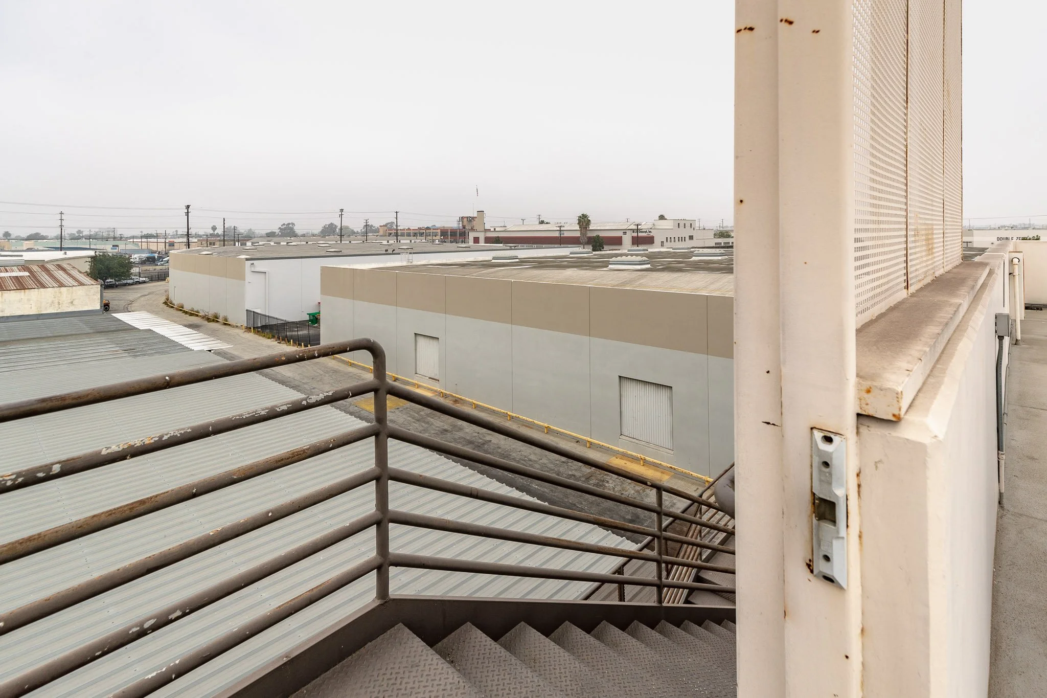View from a rooftop staircase showing industrial buildings, overcast sky, and utility poles in the distance.