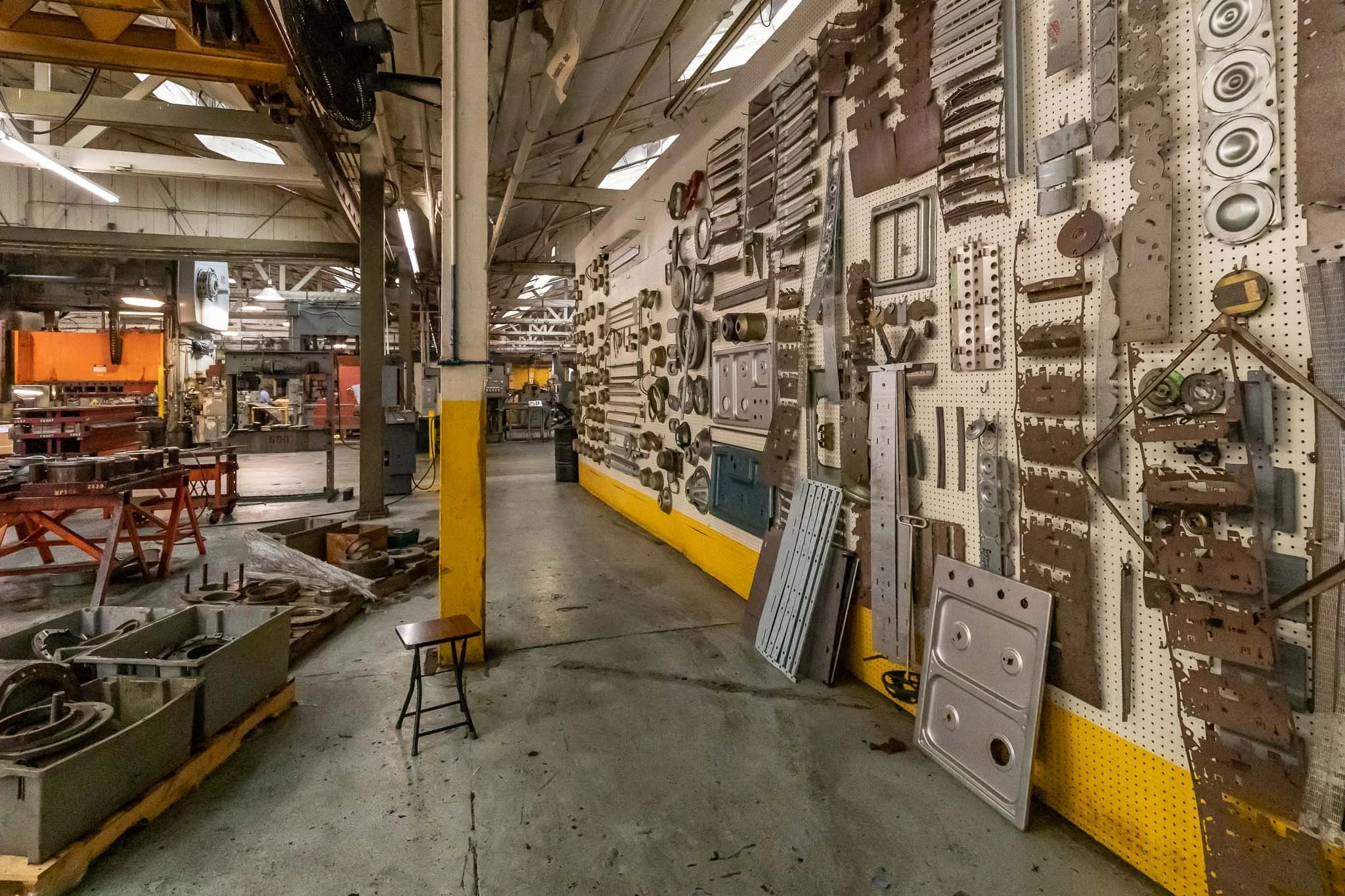 Industrial workspace with metal parts on a pegboard wall, tools, and equipment for manufacturing or machining.